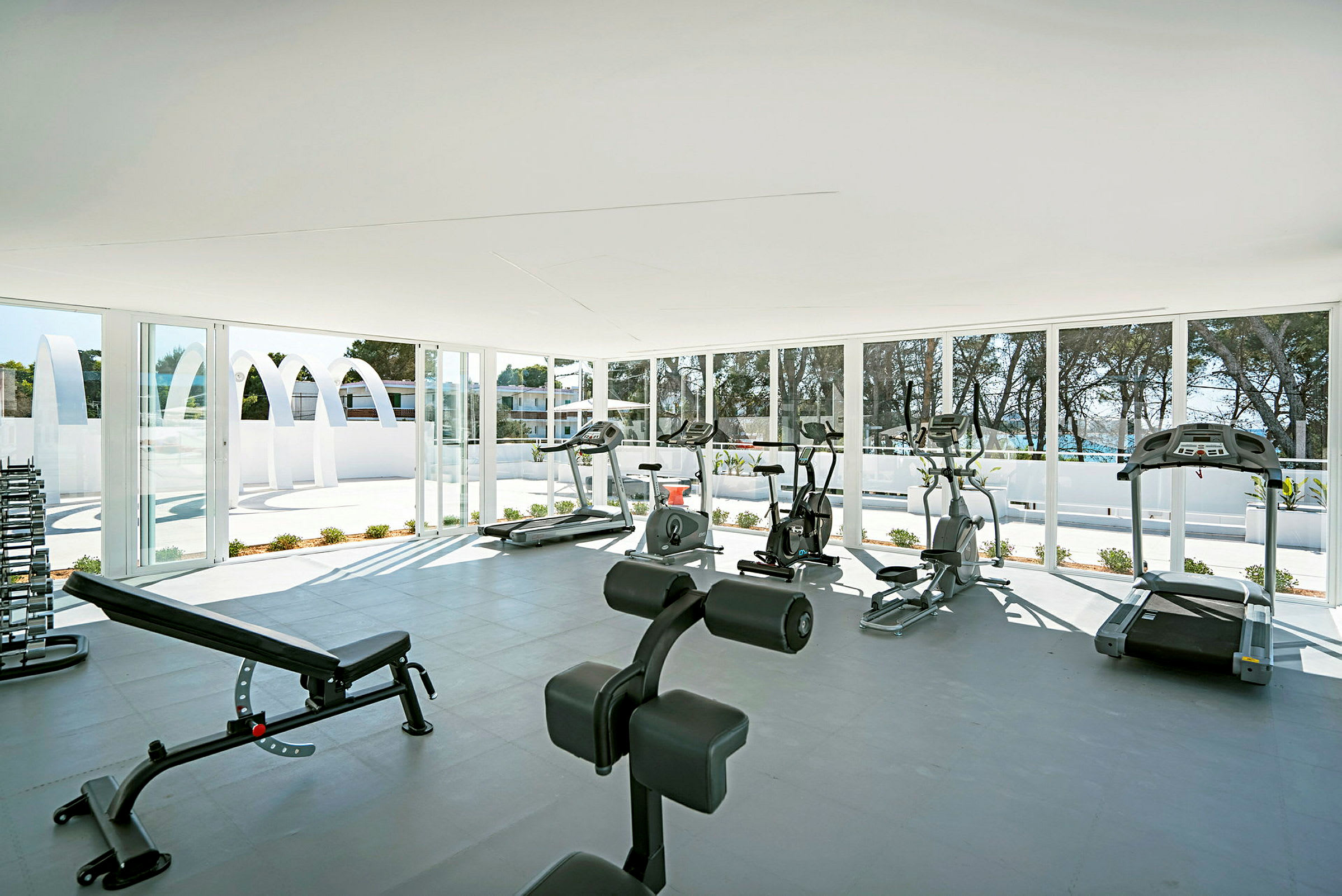 Ett ljust och rymligt gym med olika träningsmaskiner och vikter, omgärdat av fönster som visar en utomhusmiljö. (AI-genererad text)