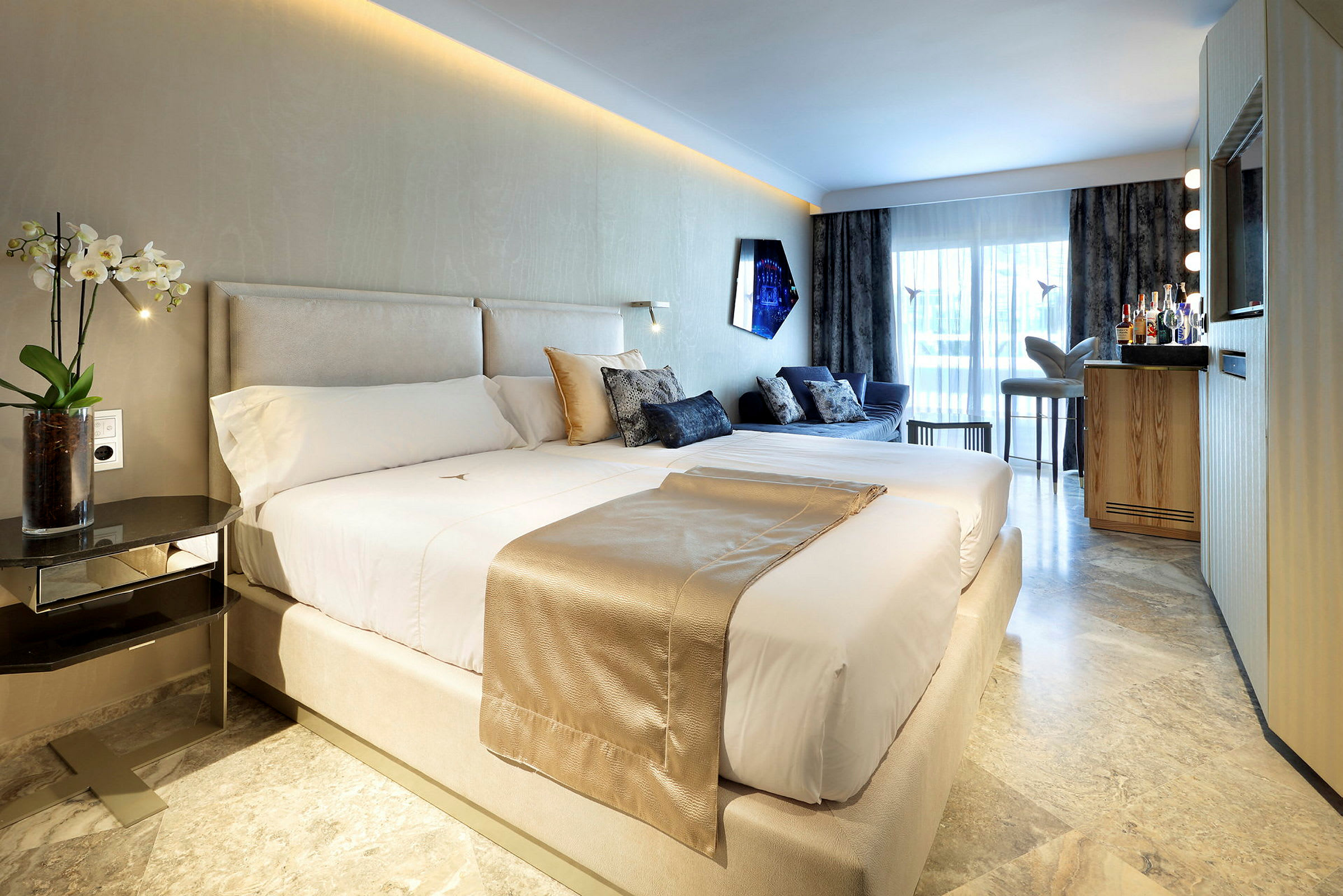 Ett modernt hotellrum med en stor säng, soffgrupp, och en minibar framför ett stort fönster. (AI-genererad text)