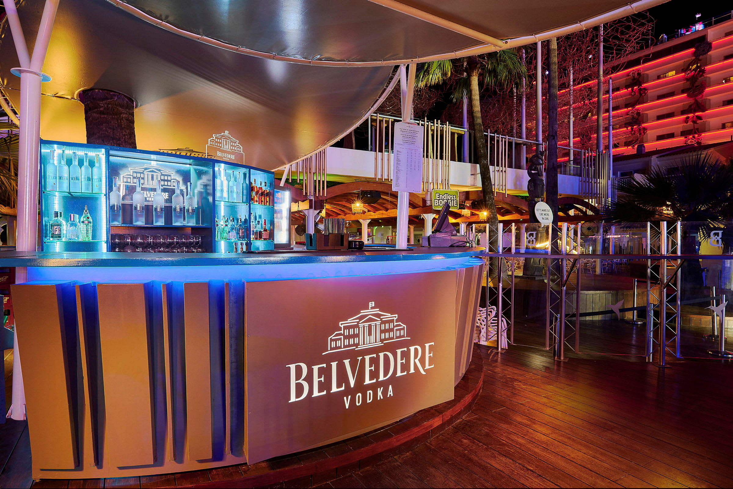 En utomhusbar med skyltning för Belvedere Vodka, belyst och med flaskor i bakgrunden. (AI-genererad text)