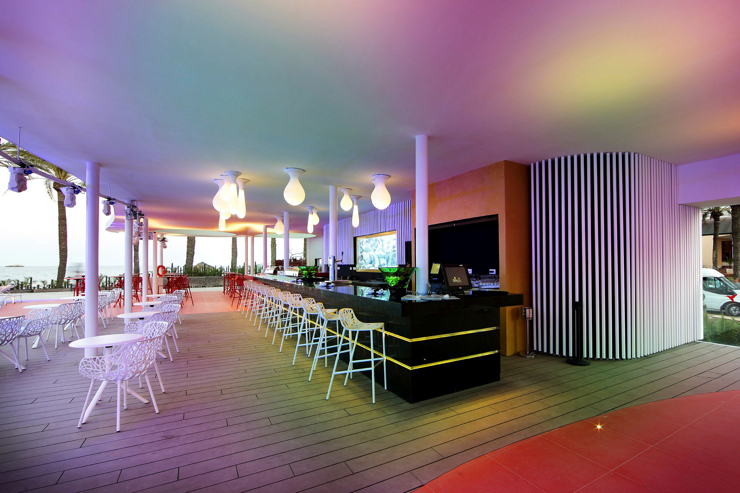 En modern, utomhus bar med färgglad belysning och sittplatser i vitt och rött. (AI-genererad text)