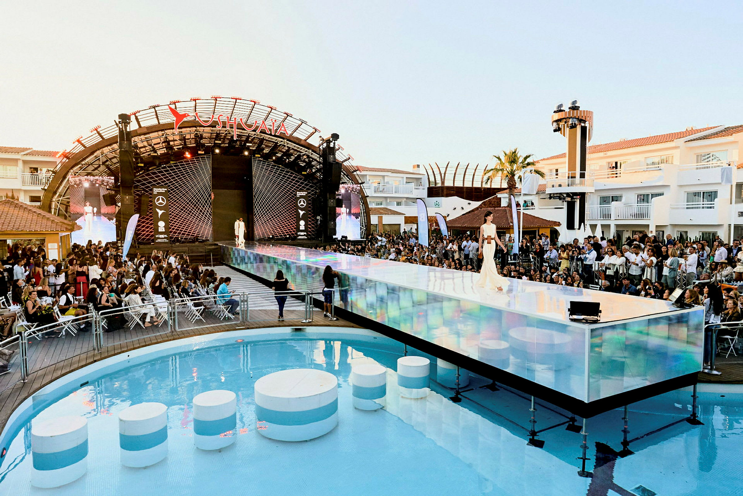 En modeuppvisning med en catwalk ovanför en swimmingpool och en publik i bakgrunden. (AI-genererad text)