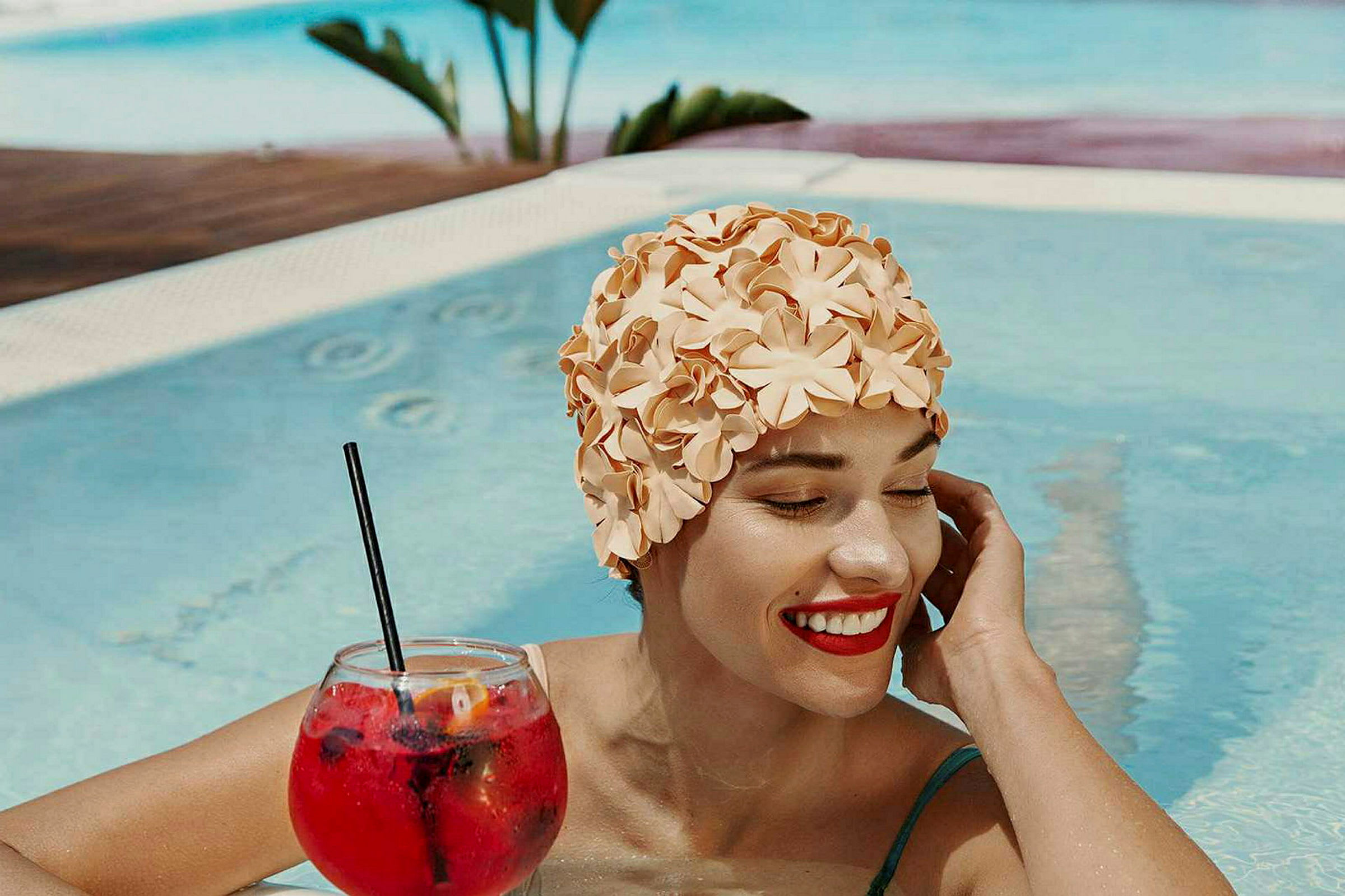 En person i en pool har på sig en blommönstrad badmössa och håller ett glas med en röd drink. (AI-genererad text)