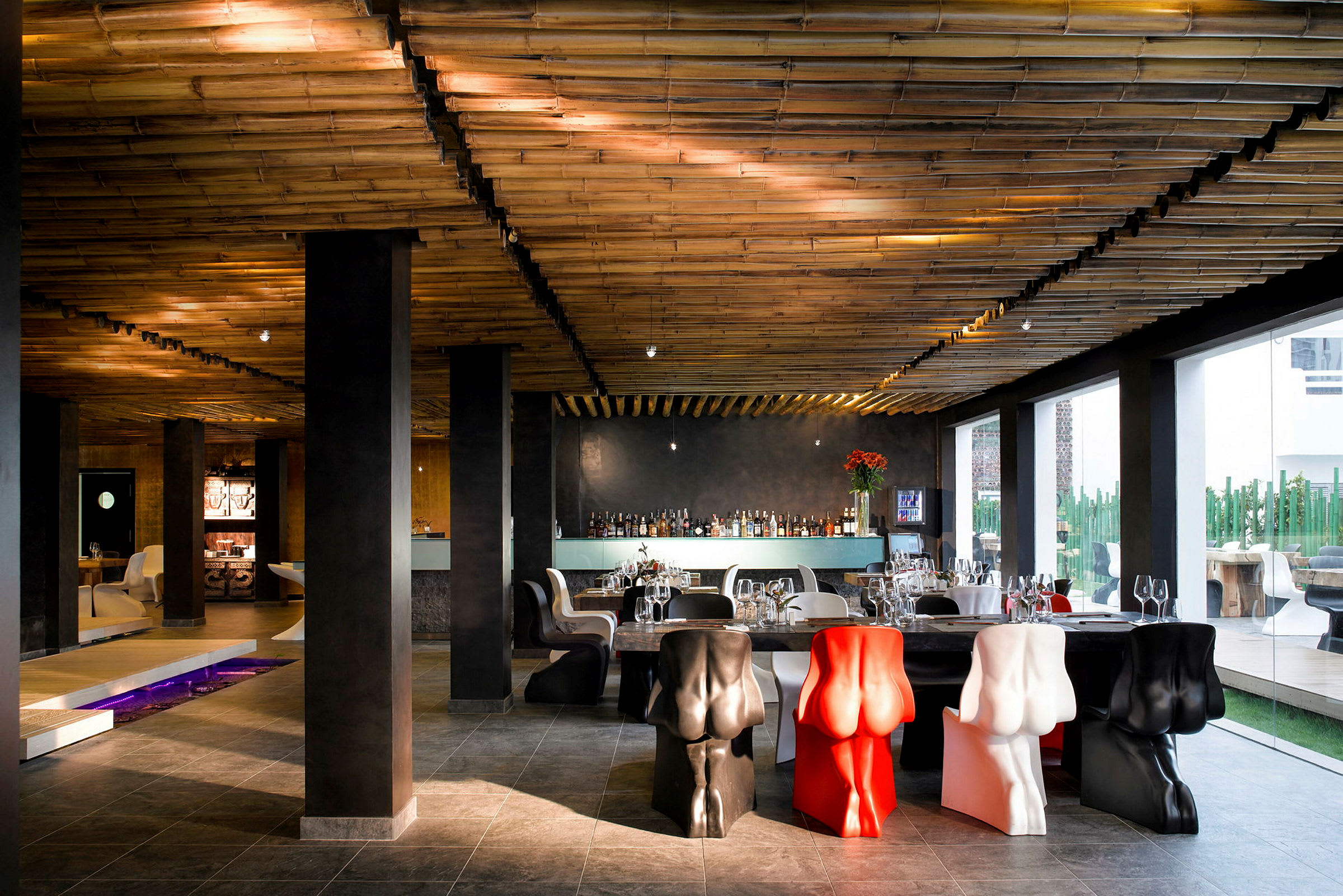 Restaurang med dekorativa stolar, ett bambutak och stora fönster som släpper in ljus. (AI-genererad text)