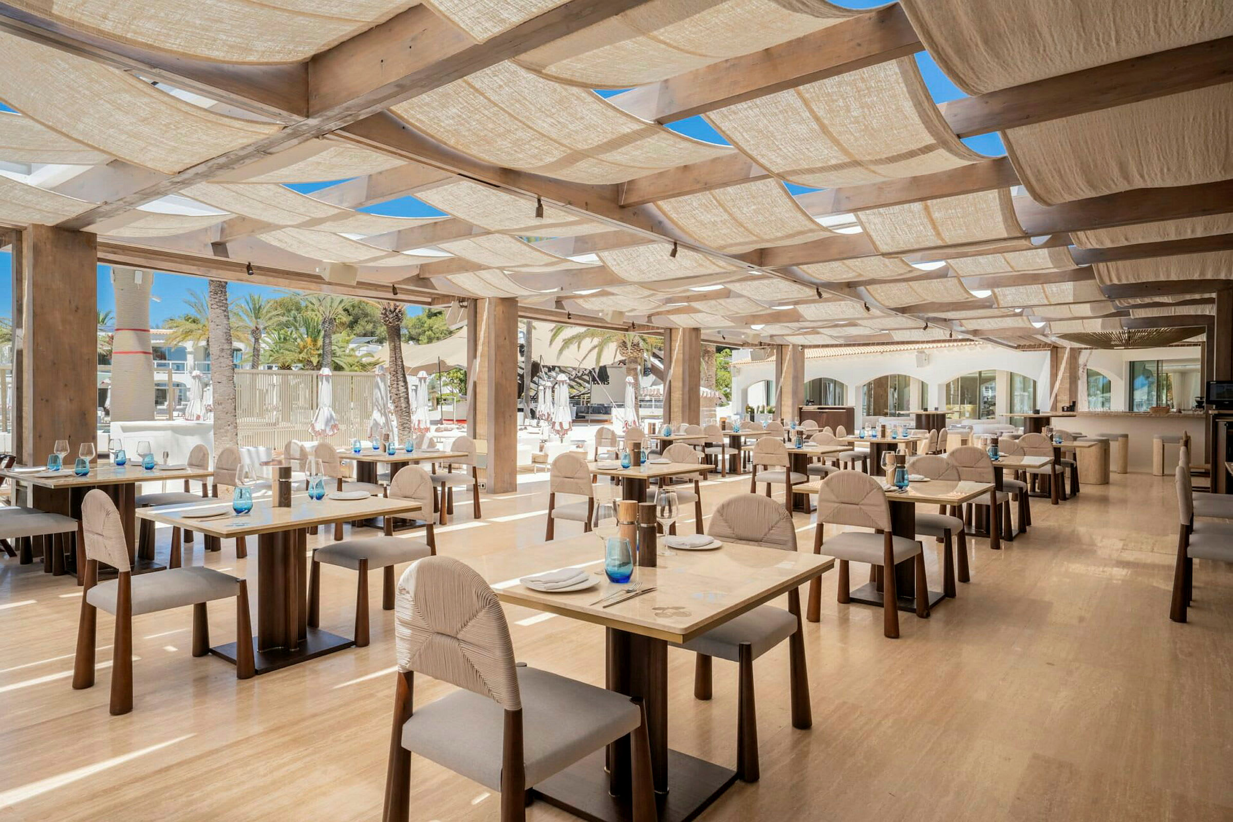En restaurang med bord och stolar i trä, väl upplyst med naturligt ljus. (AI-genererad text)