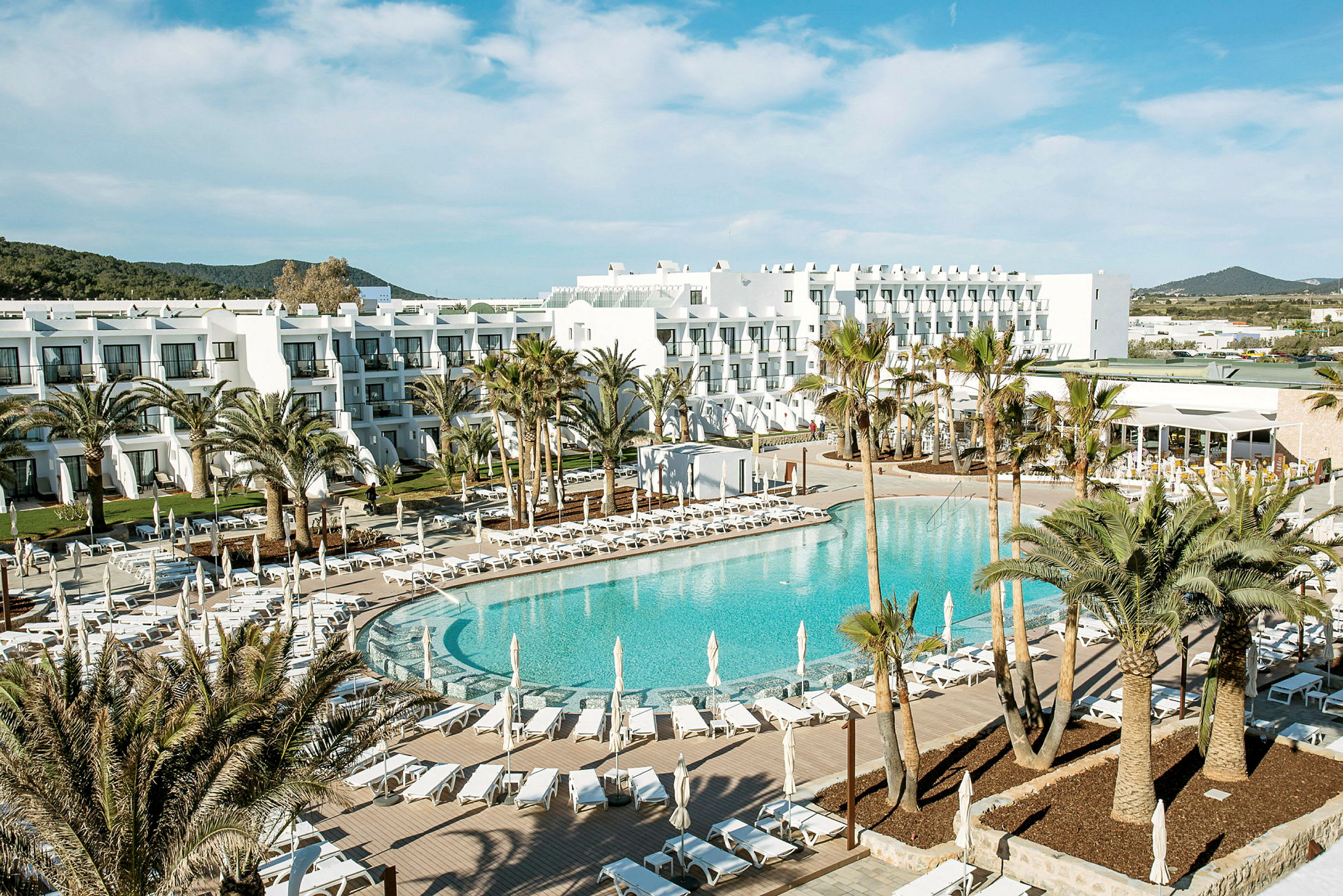 Ett hotellområde med en stor pool, omgiven av solstolar, parasoller och palmer. (AI-genererad text)