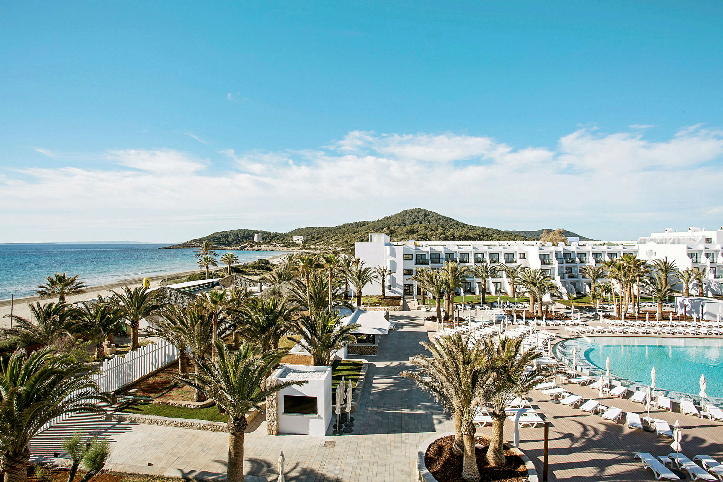 Ett hotellområde vid stranden med pool, palmer och en byggnad i vitt. (AI-genererad text)