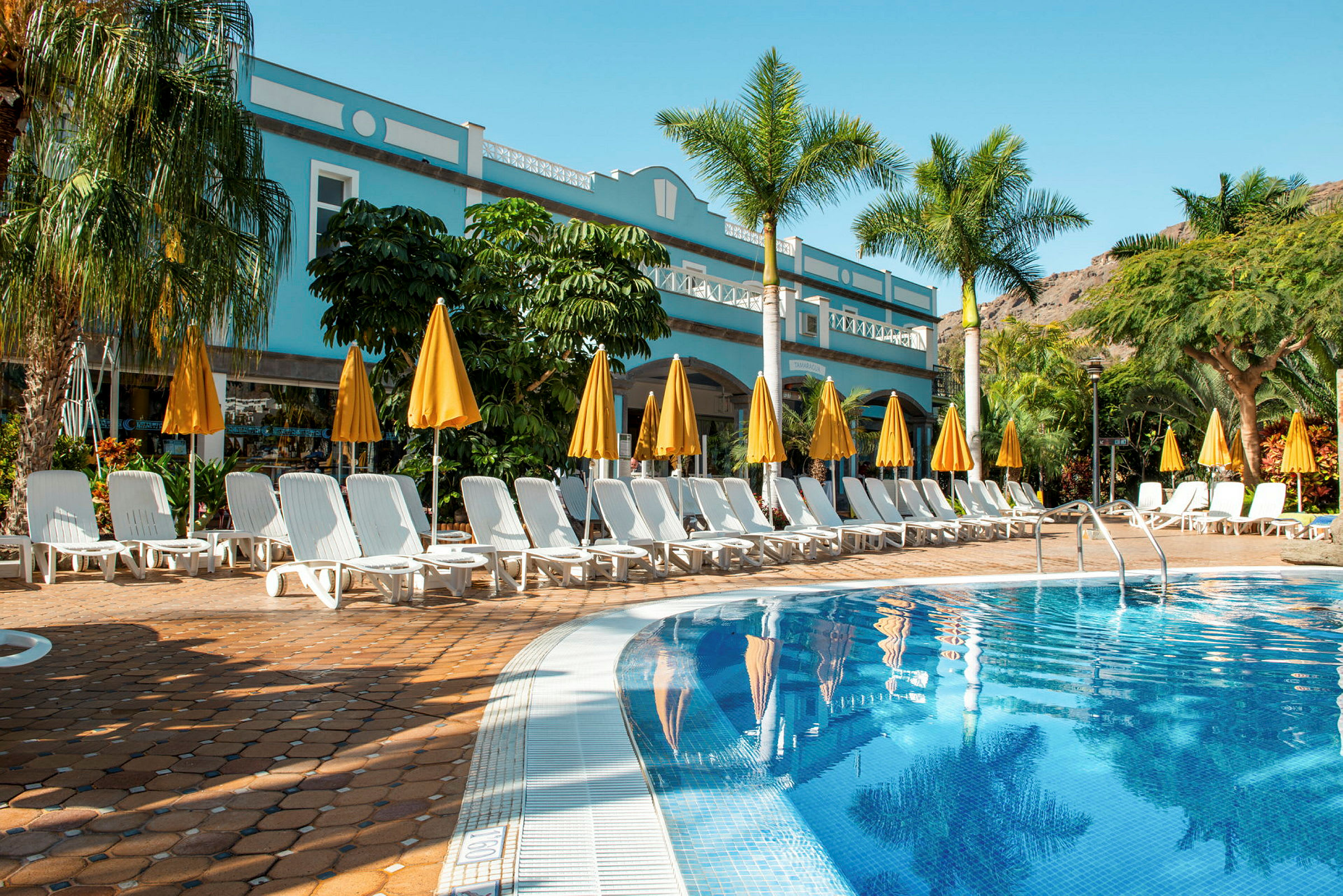 Utomhuspool vid ett hotell med solstolar och gula parasoll. (AI-genererad text)