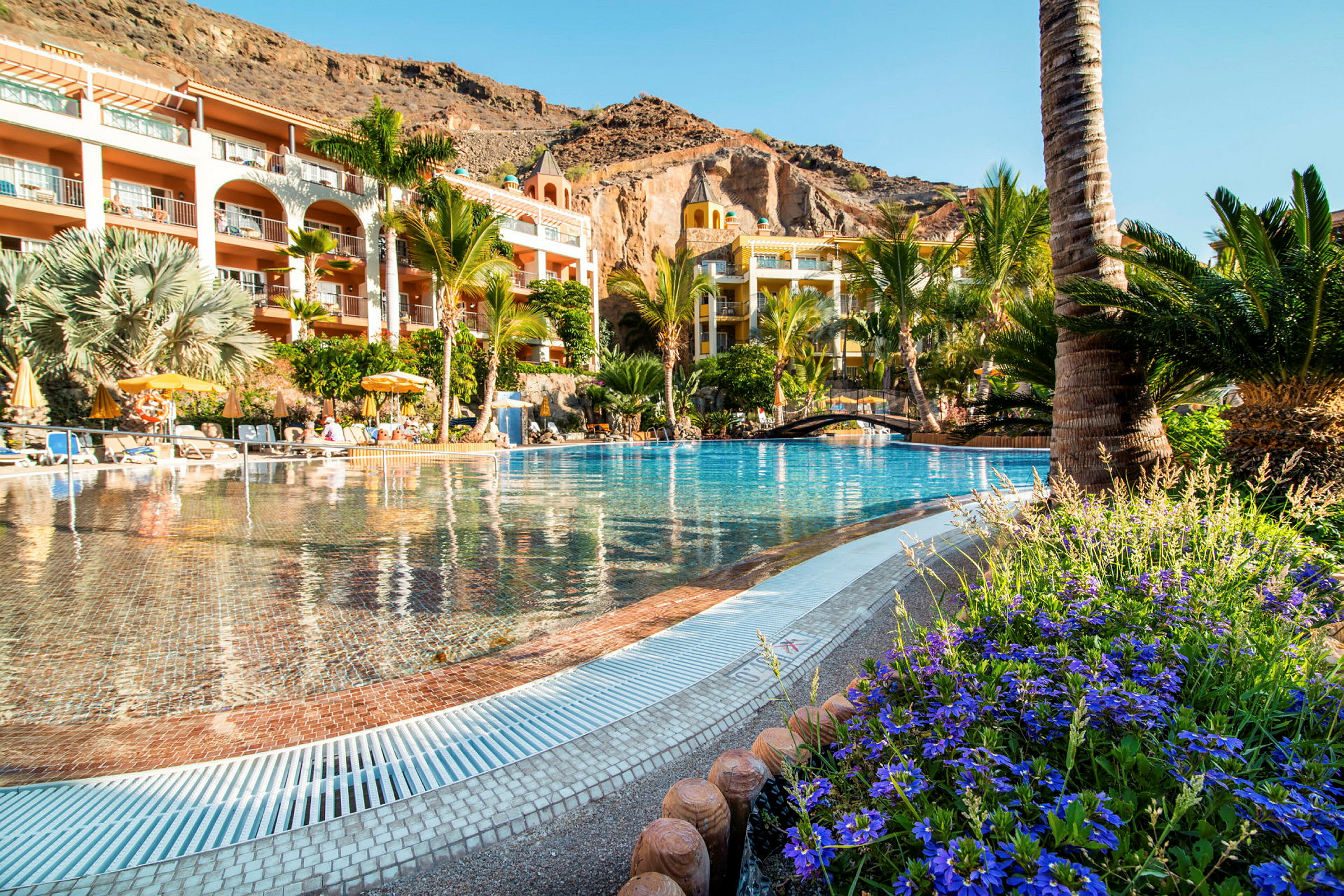 En bild av en pool vid ett hotell omgivet av grönska och berg. (AI-genererad text)