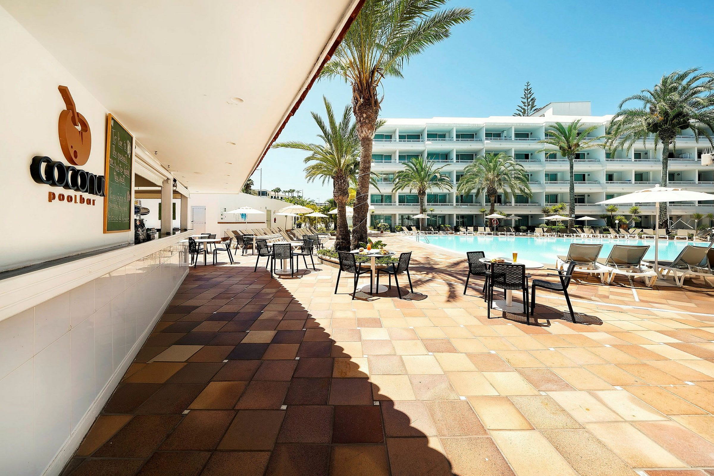 Ett poolområde vid ett hotell med en uteservering och solstolar nära en pool. (AI-genererad text)