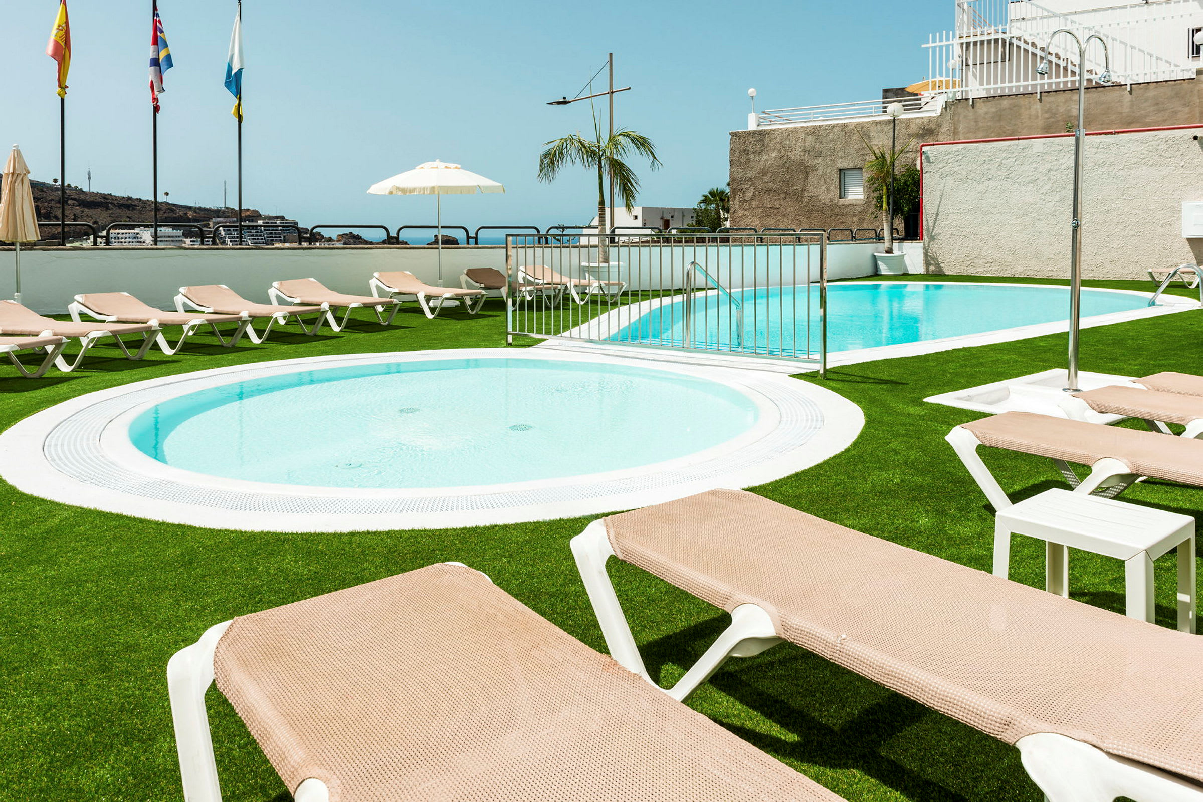 En pool och barnpool med solstolar och parasoll på konstgräs. (AI-genererad text)