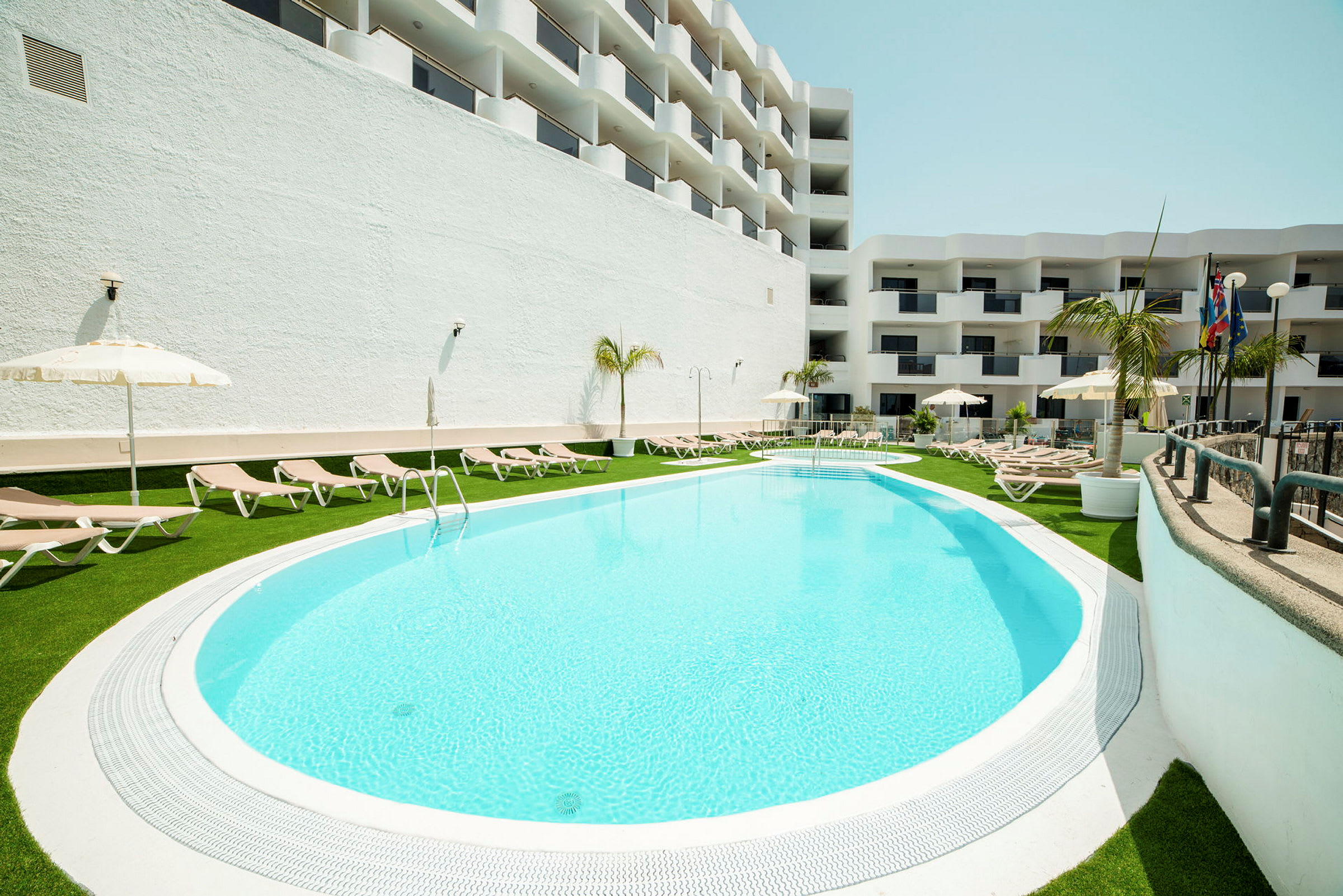 En hotellpool omgiven av solstolar och parasoller. (AI-genererad text)