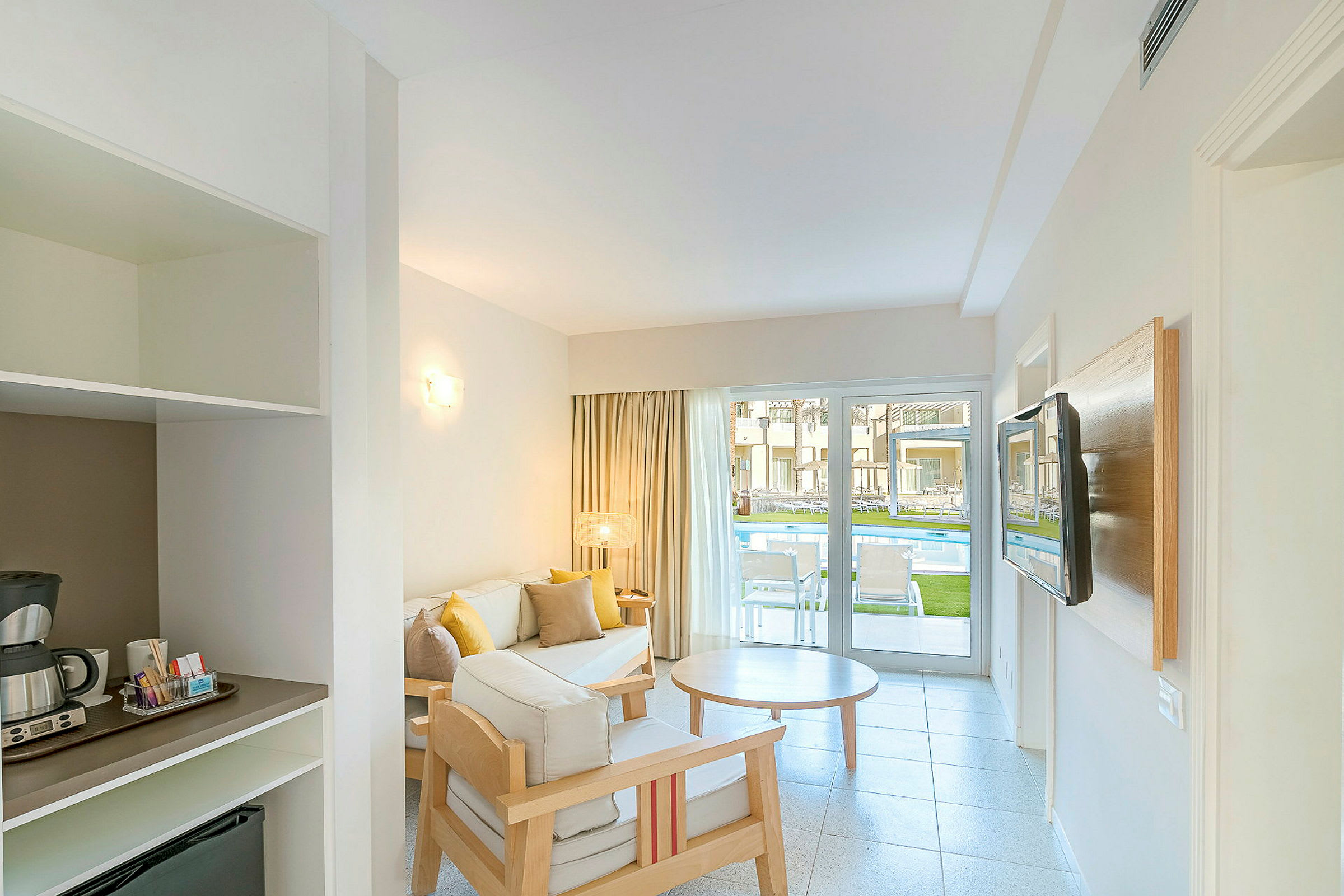 Hotellrum med sittgrupp och utsikt mot poolen genom en glasdörr. (AI-genererad text)