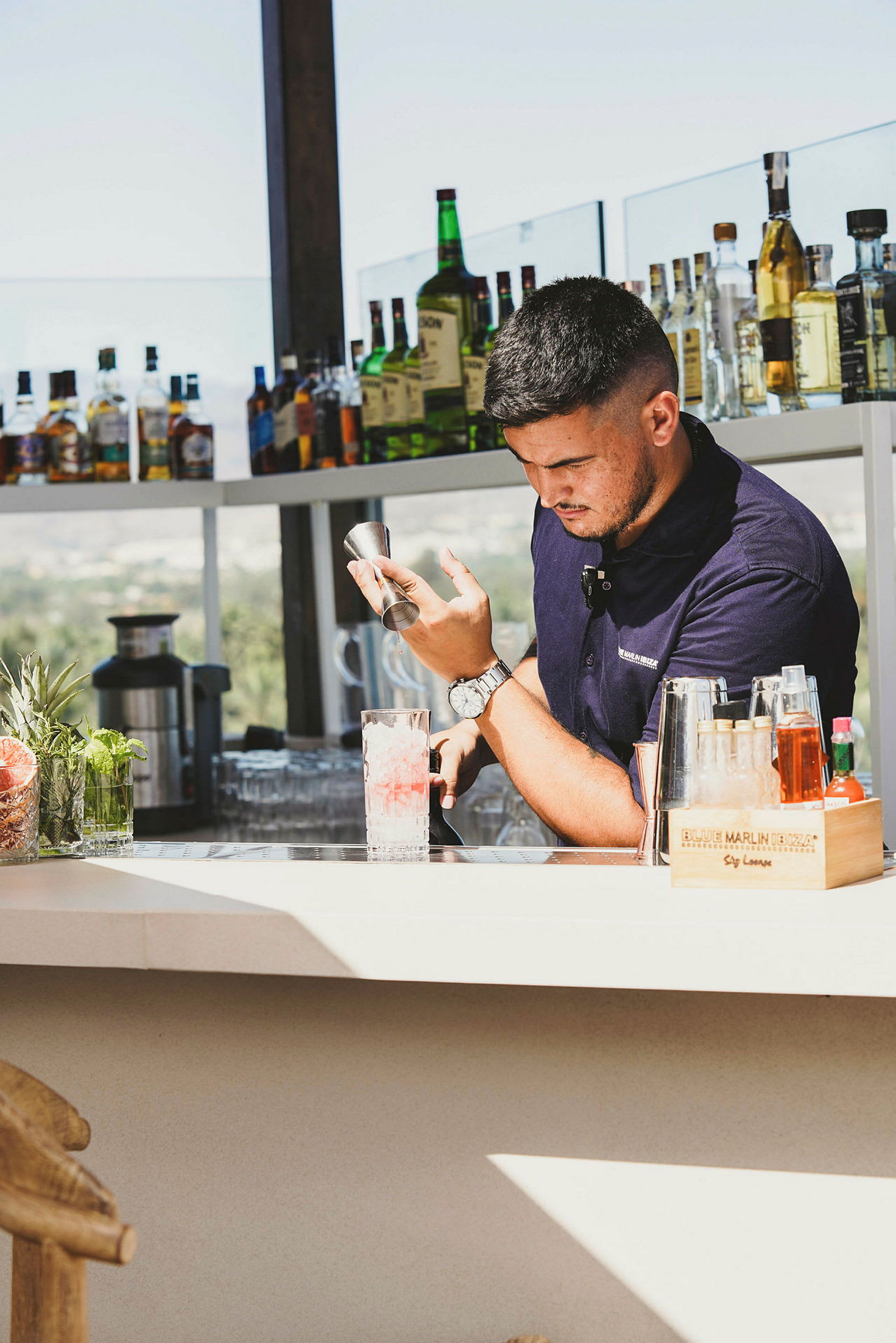 En bartender vid en bar med flaskor och drycker på hyllor. (AI-genererad text)