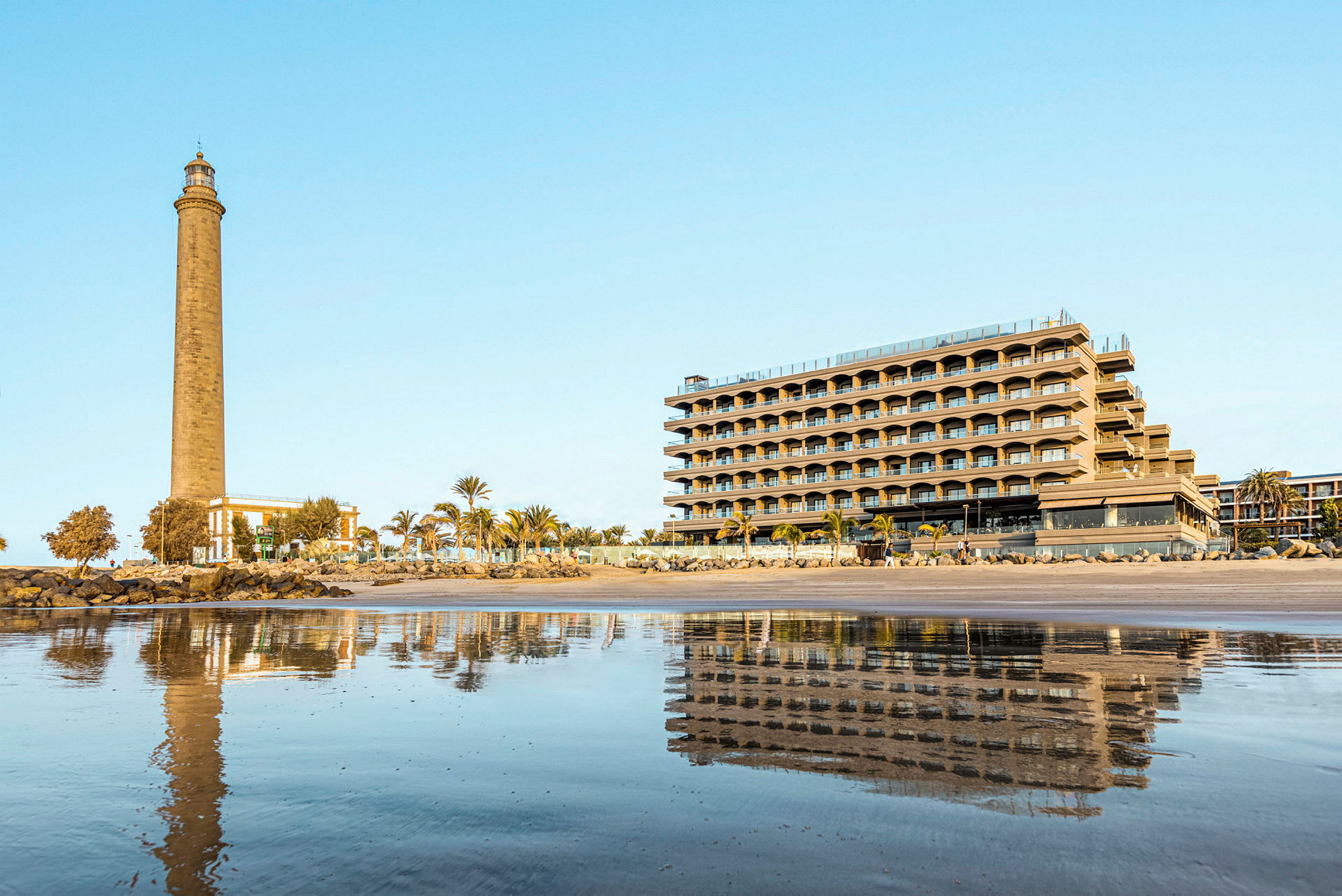 En fyr och en byggnad vid stranden med reflektioner i vatten. (AI-genererad text)