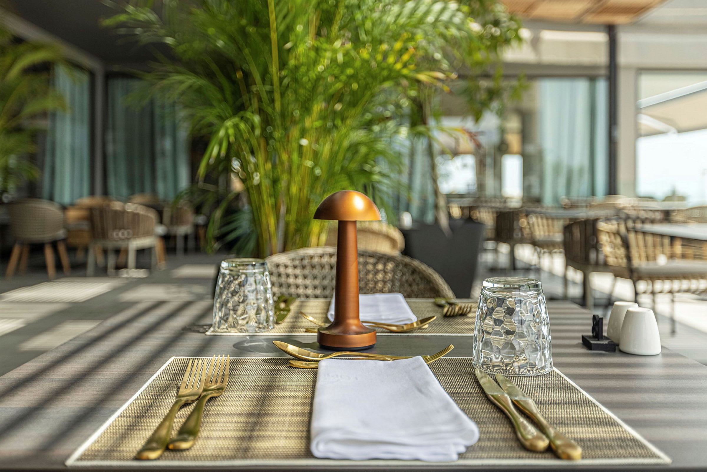 Bord i ett restaurangområde är dukat med glas, bestick och servetter. En dekorativ lampa är placerad i mitten. (AI-genererad text)
