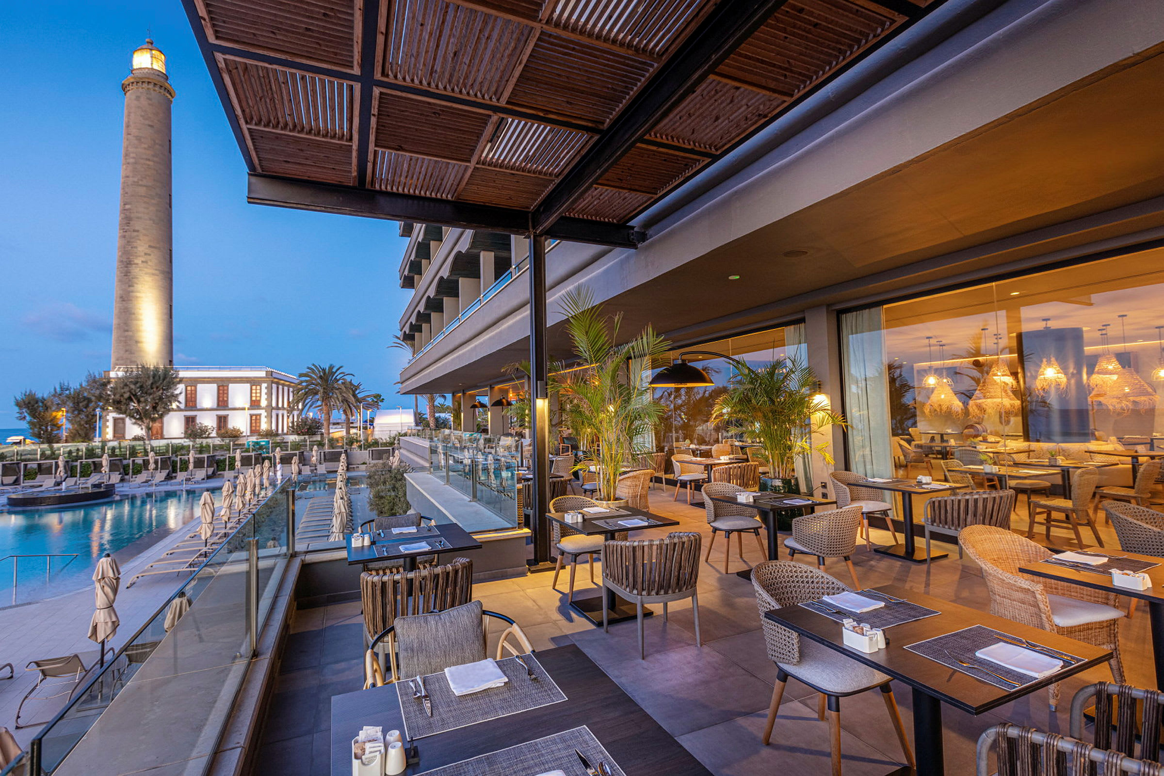 Restaurang med utomhusbord vid ett hotell, en fyr i bakgrunden. (AI-genererad text)