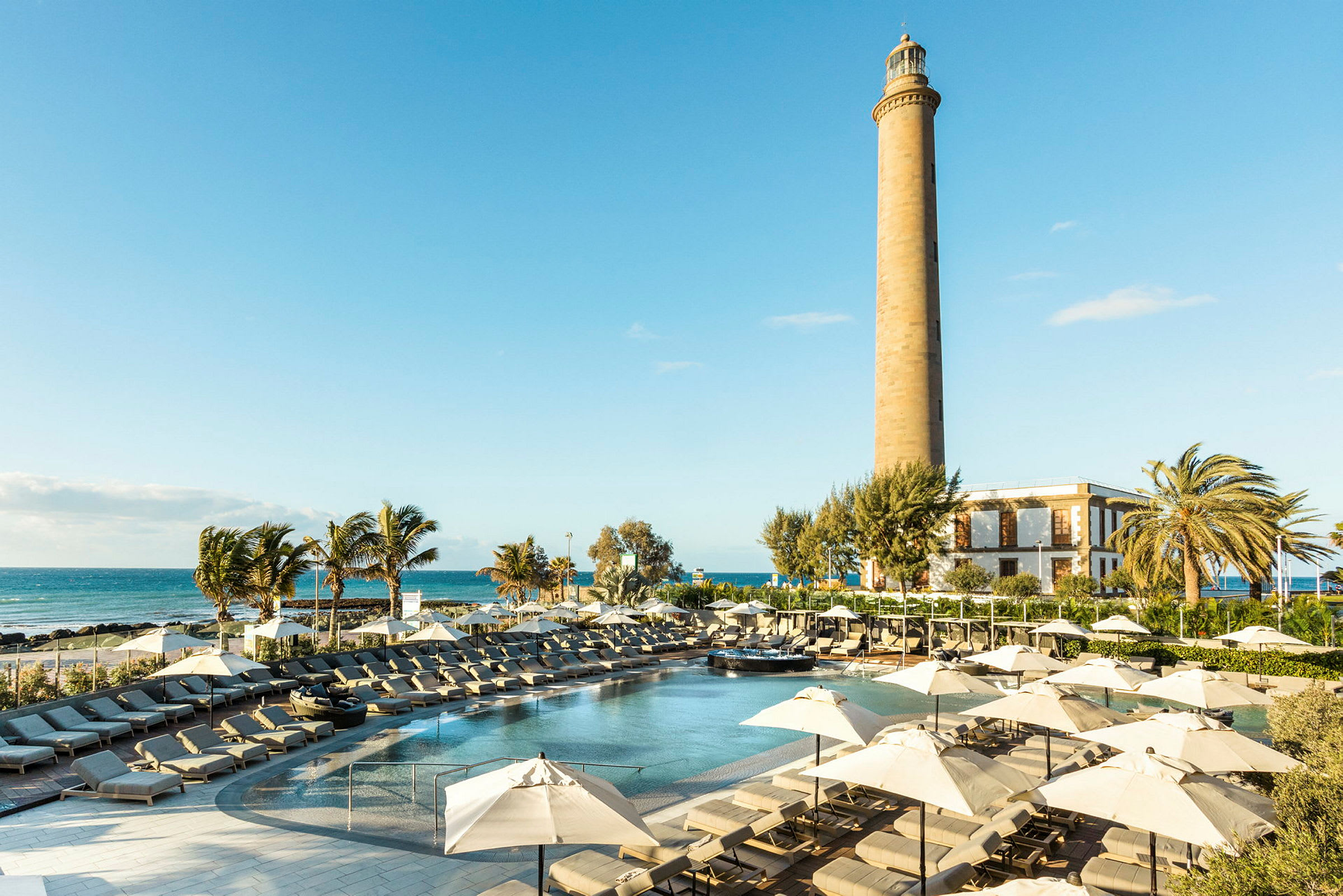 En solig resort med pool, solstolar och parasoller samt en fyr i bakgrunden. (AI-genererad text)