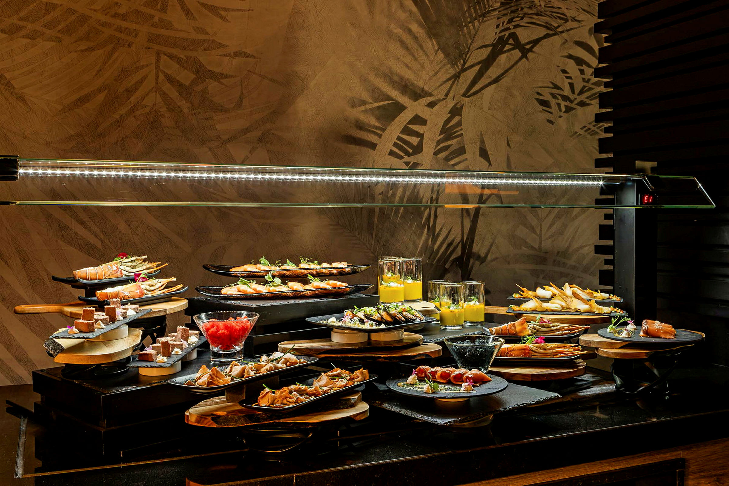 Ett buffébord med olika maträtter och desserter upplagda på tallrikar och glas, under en glashuva. (AI-genererad text)