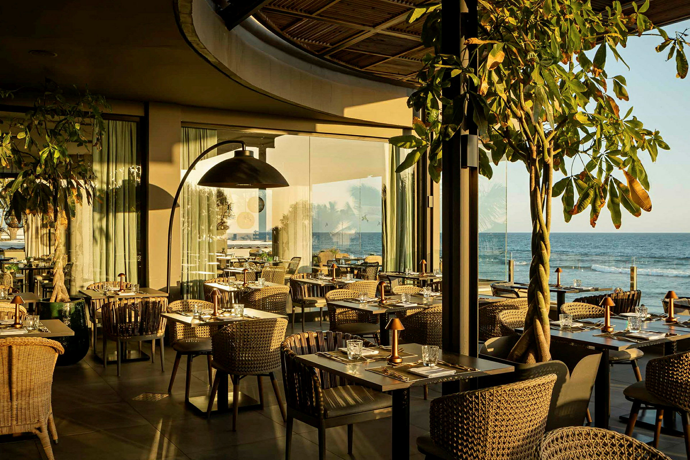 En restaurang med bord och stolar nära havet, med solen som lyser in. (AI-genererad text)