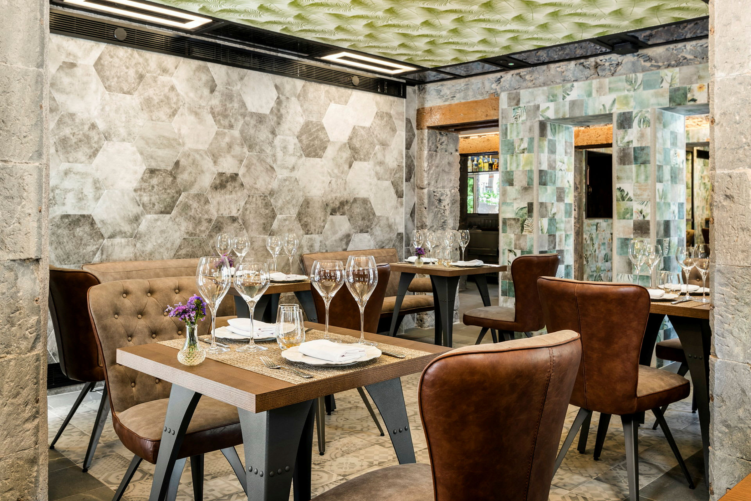 En restaurang med flera bord, dukade med glas och servetter. Stolarna har brunt läder, och väggarna har geometriska mönster. (AI-genererad text)