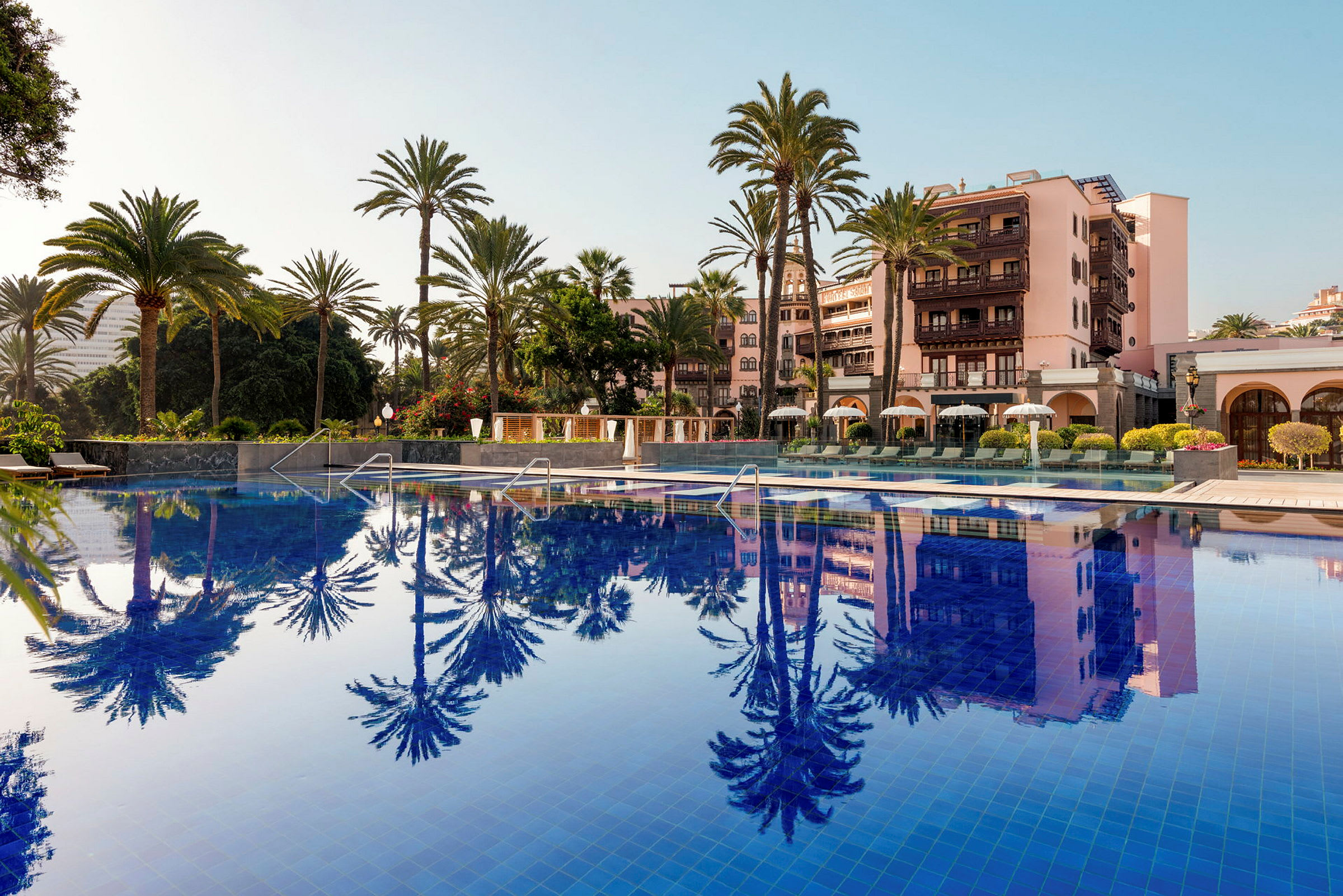 Ett hotellområde med en stor pool, palmträd och rosa byggnader. (AI-genererad text)