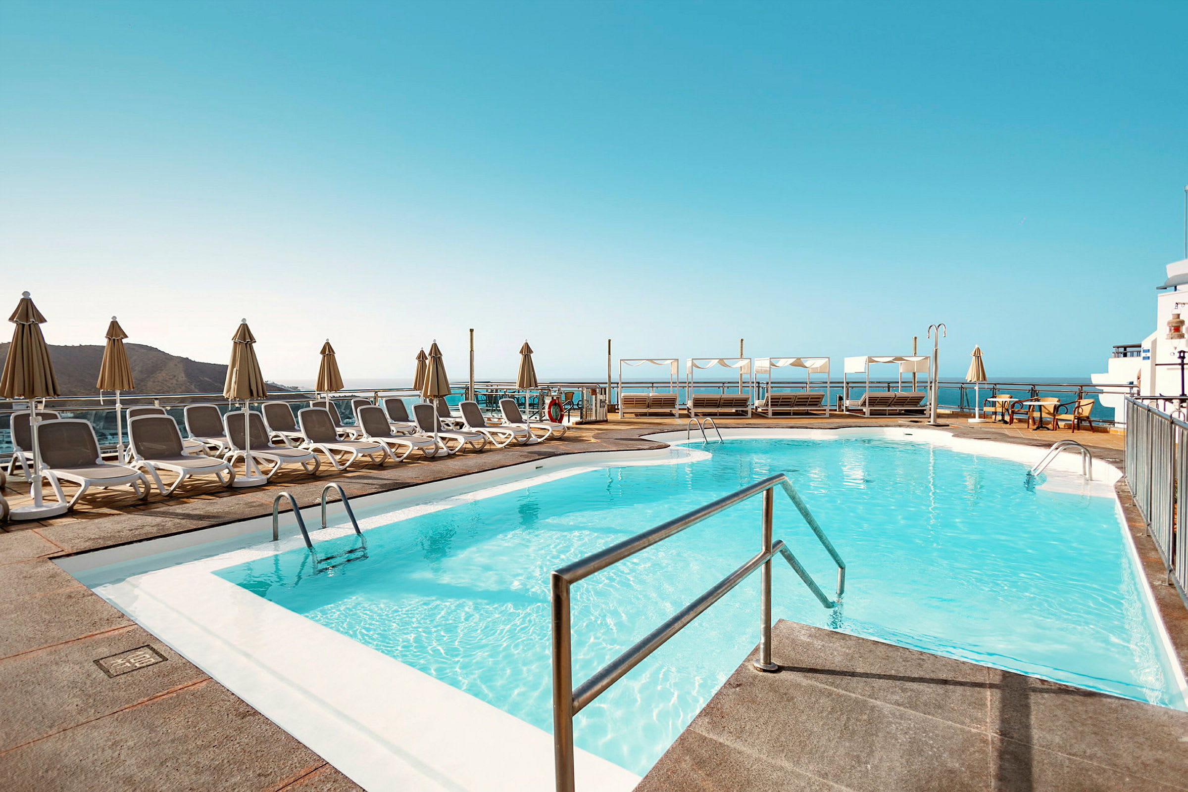 Poolområde med solstolar och parasoller samt utsikt över havet. (AI-genererad text)