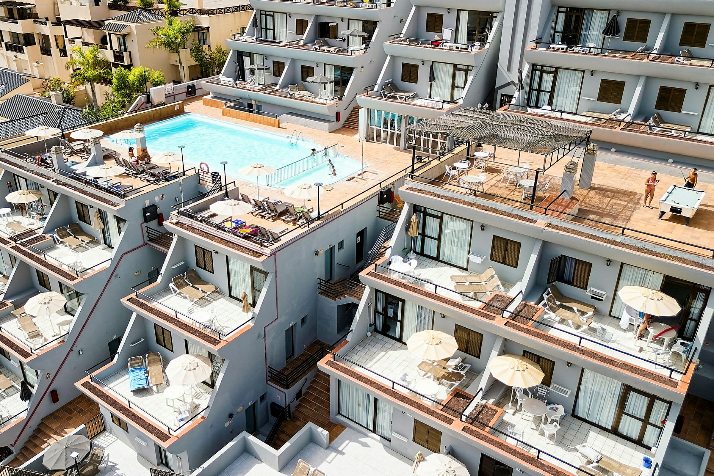 Bild av en byggnad med lägenheter, en pool och terrasser med solstolar. (AI-genererad text)