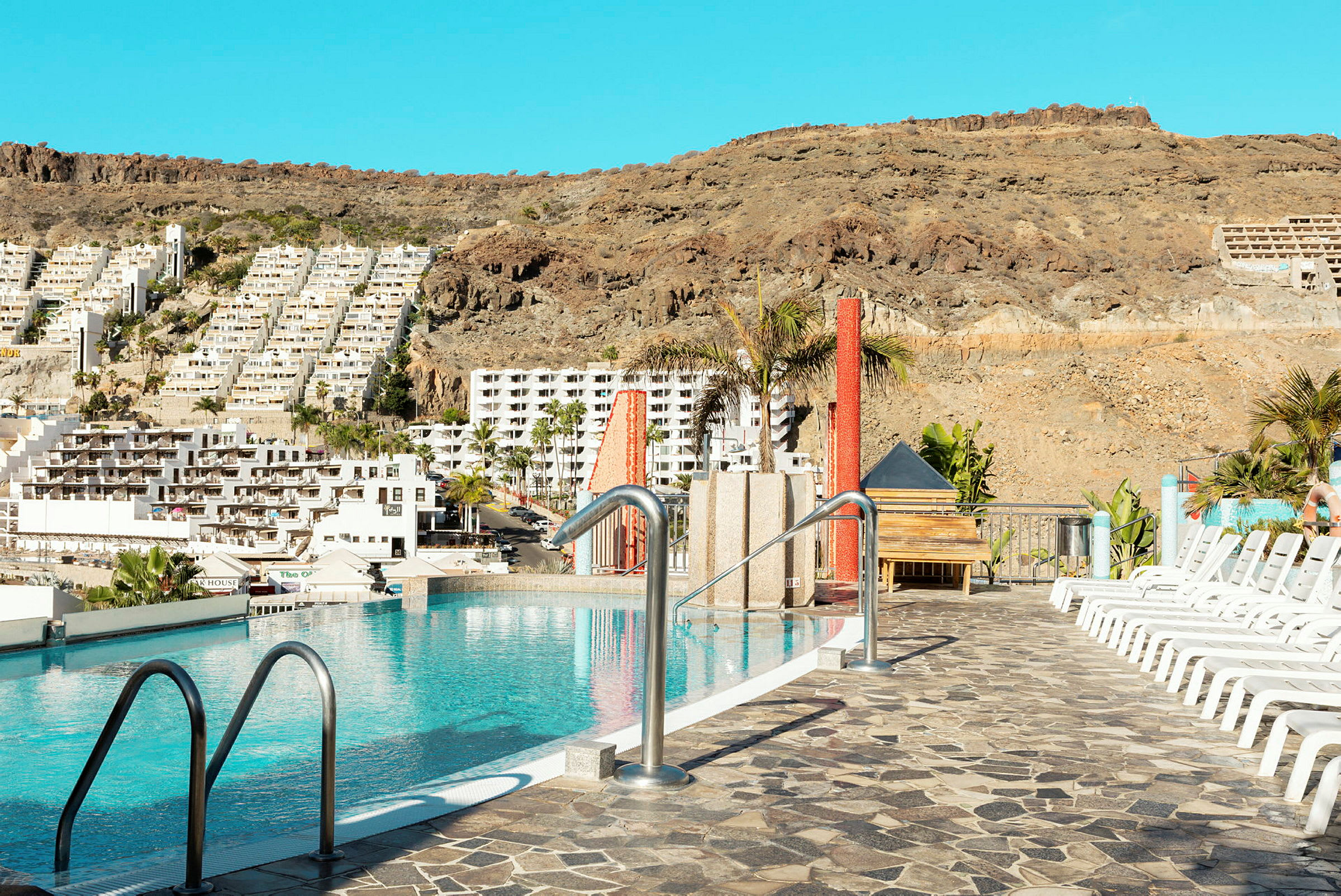 Bild av en pool med utsikt över en brant sluttning fylld med vita byggnader i bakgrunden. (AI-genererad text)