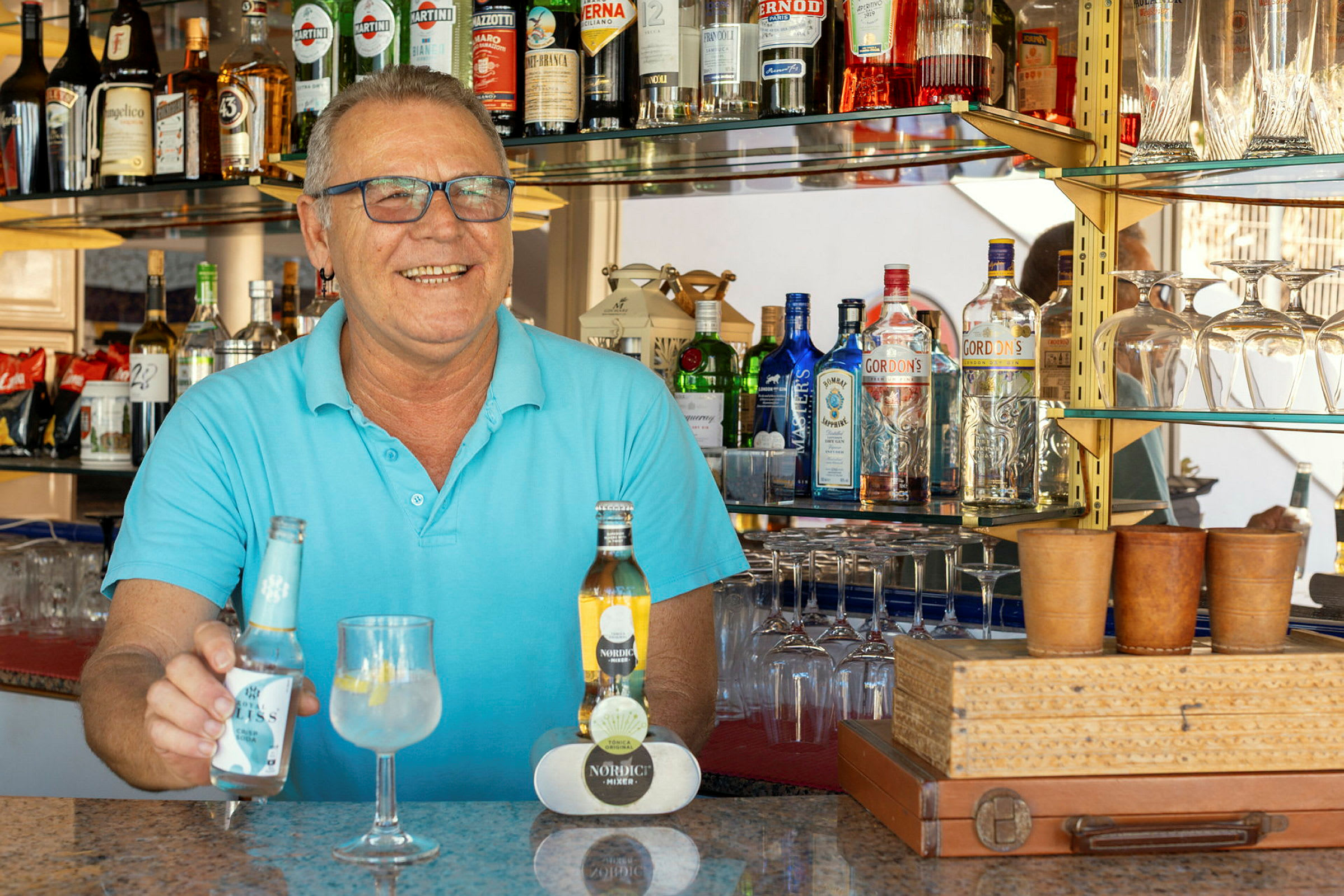 En bar med diverse spritflaskor på hyllor och ett serveringsbord med drycker. (AI-genererad text)
