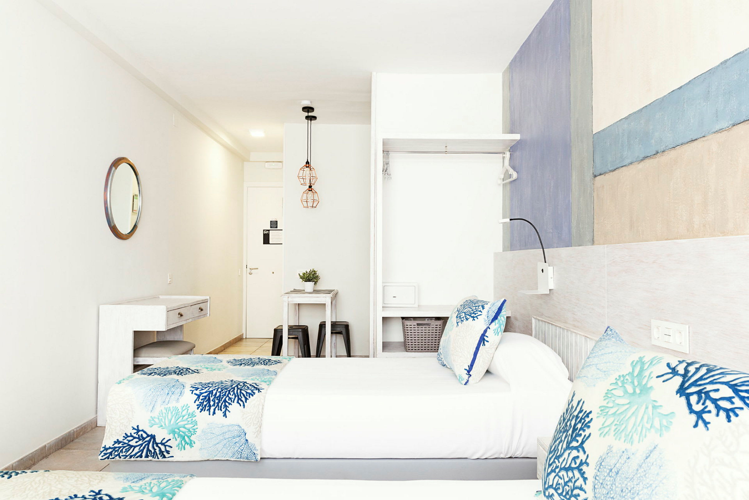 Två enkelsängar med blåmönstrade sängkläder i ett ljus och modernt hotellrum. (AI-genererad text)