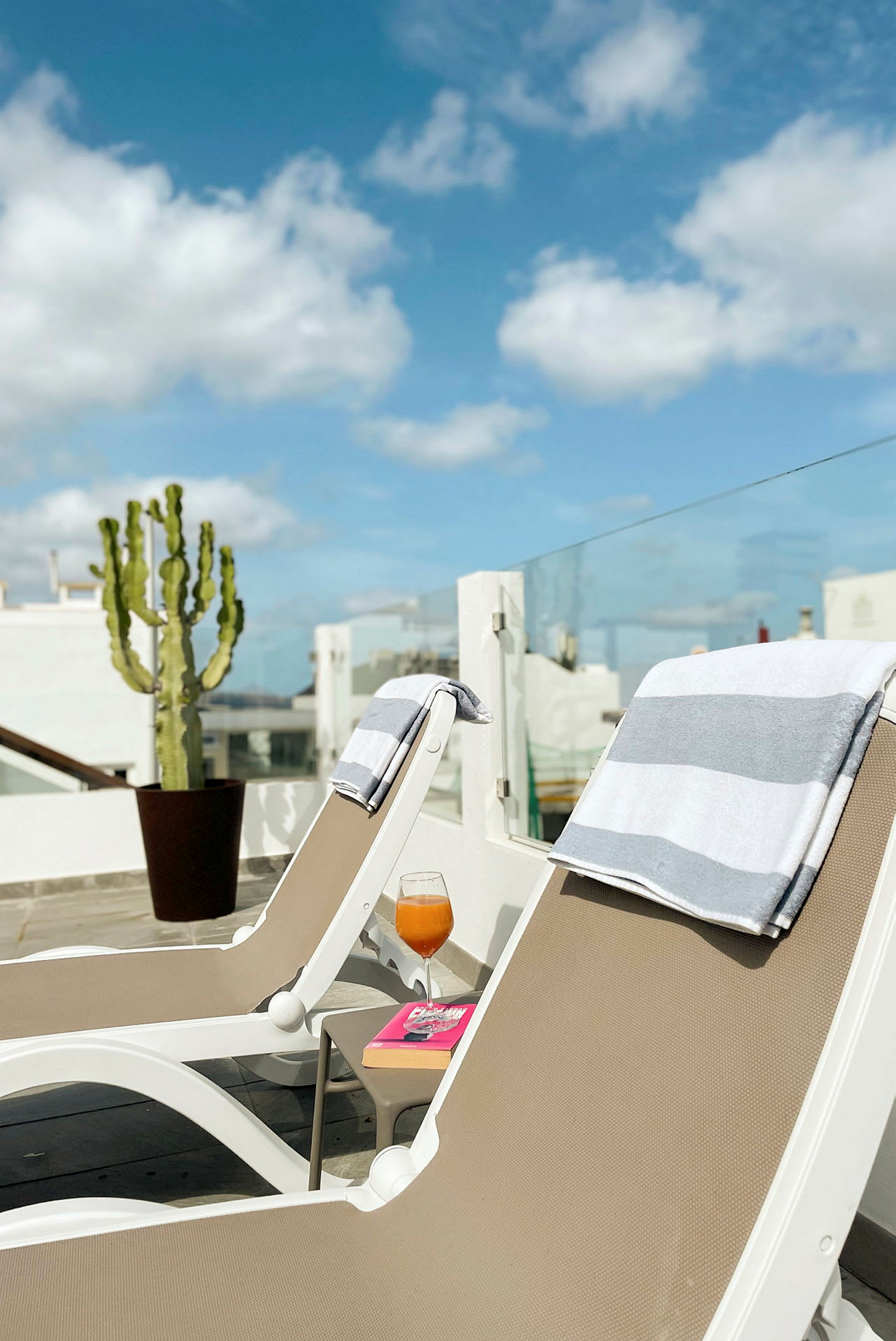 Två solstolar med handdukar på en terrass, en drink och en bok på ett bord bredvid. (AI-genererad text)