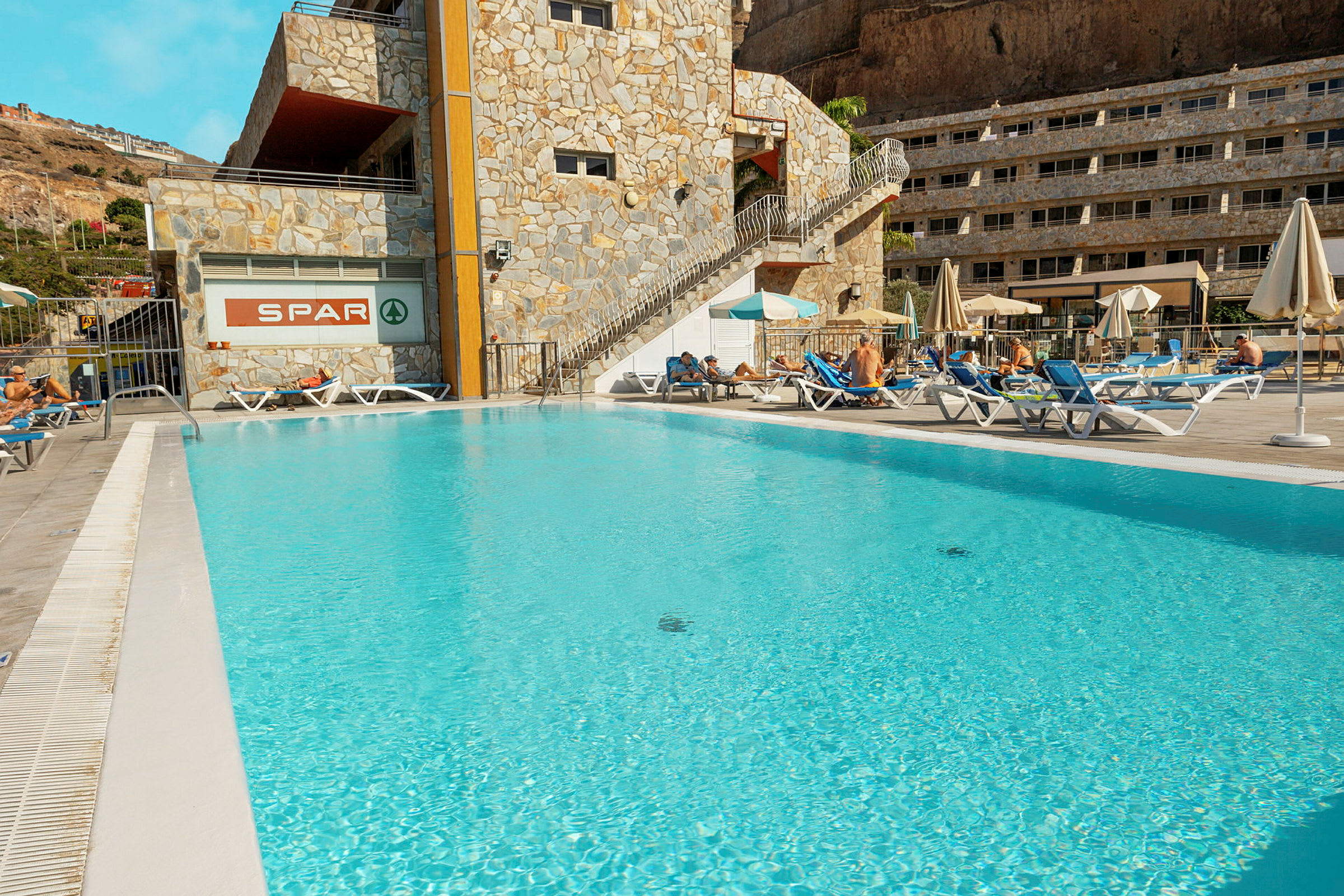 Utomhuspool vid hotell med solstolar och parasoller. (AI-genererad text)