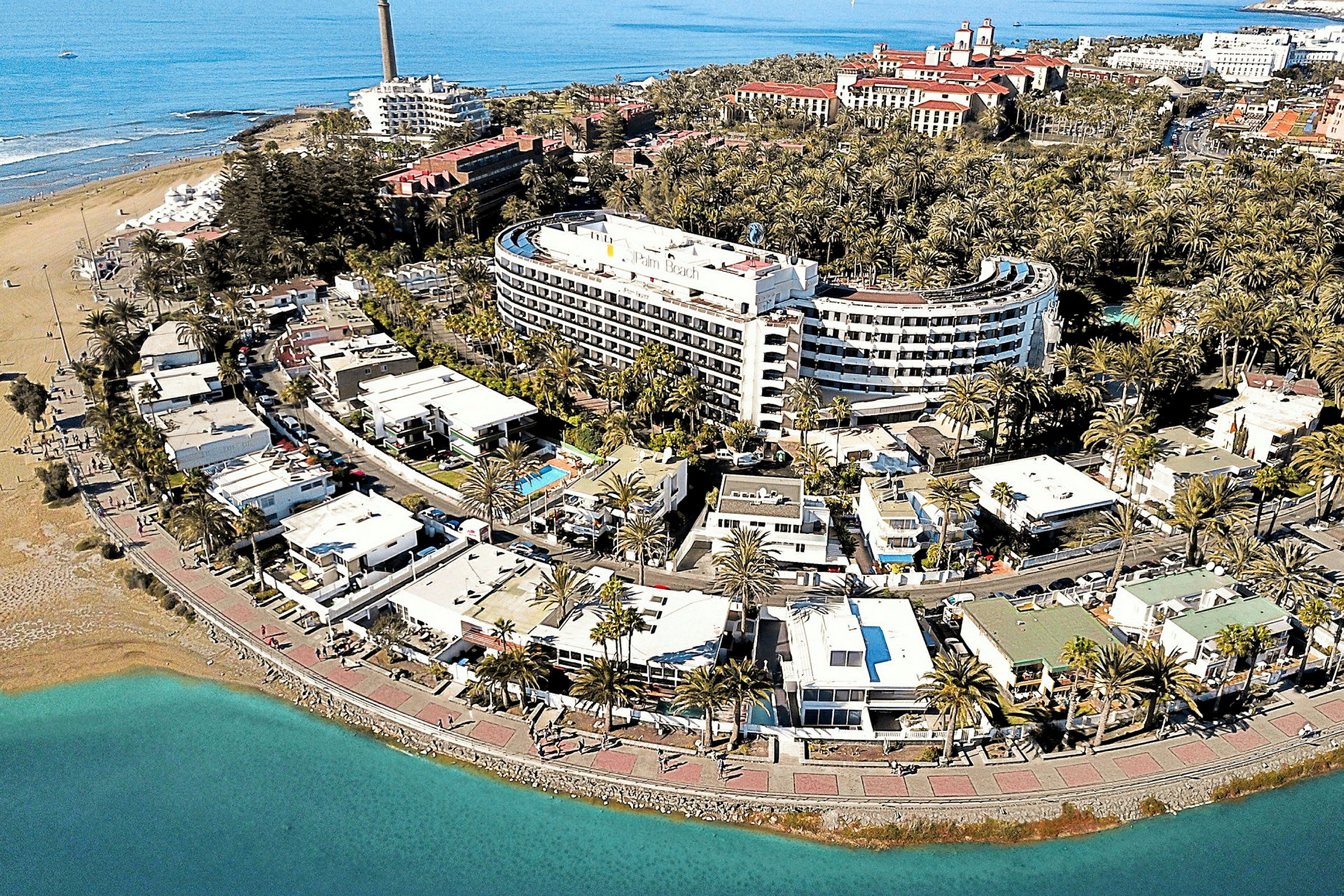 Flygbild av en kuststad med hotell, palmer och strand. (AI-genererad text)