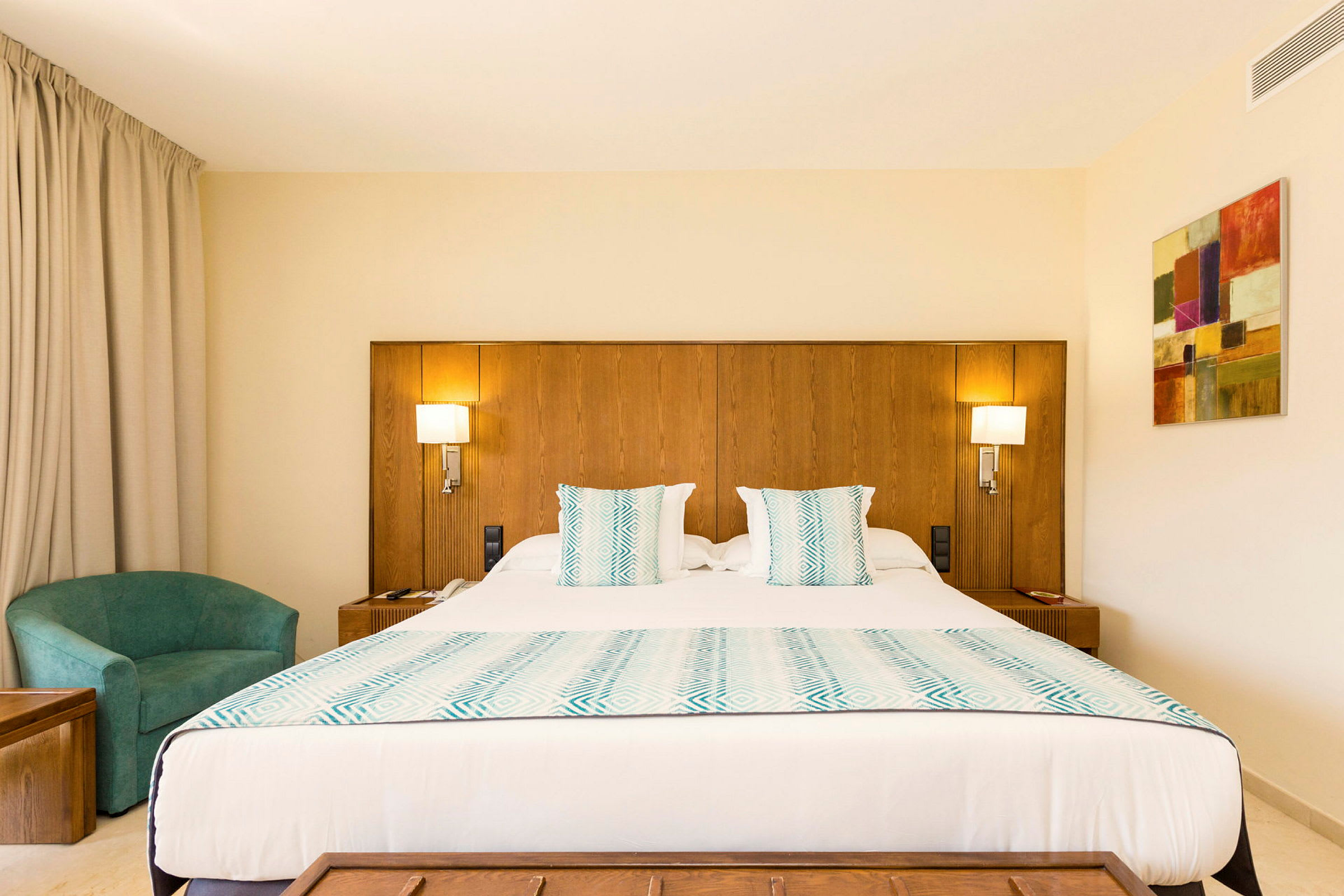 Interiör av ett hotellrum med en stor säng, träpanel på väggen, turkosa textilier och möbler. (AI-genererad text)