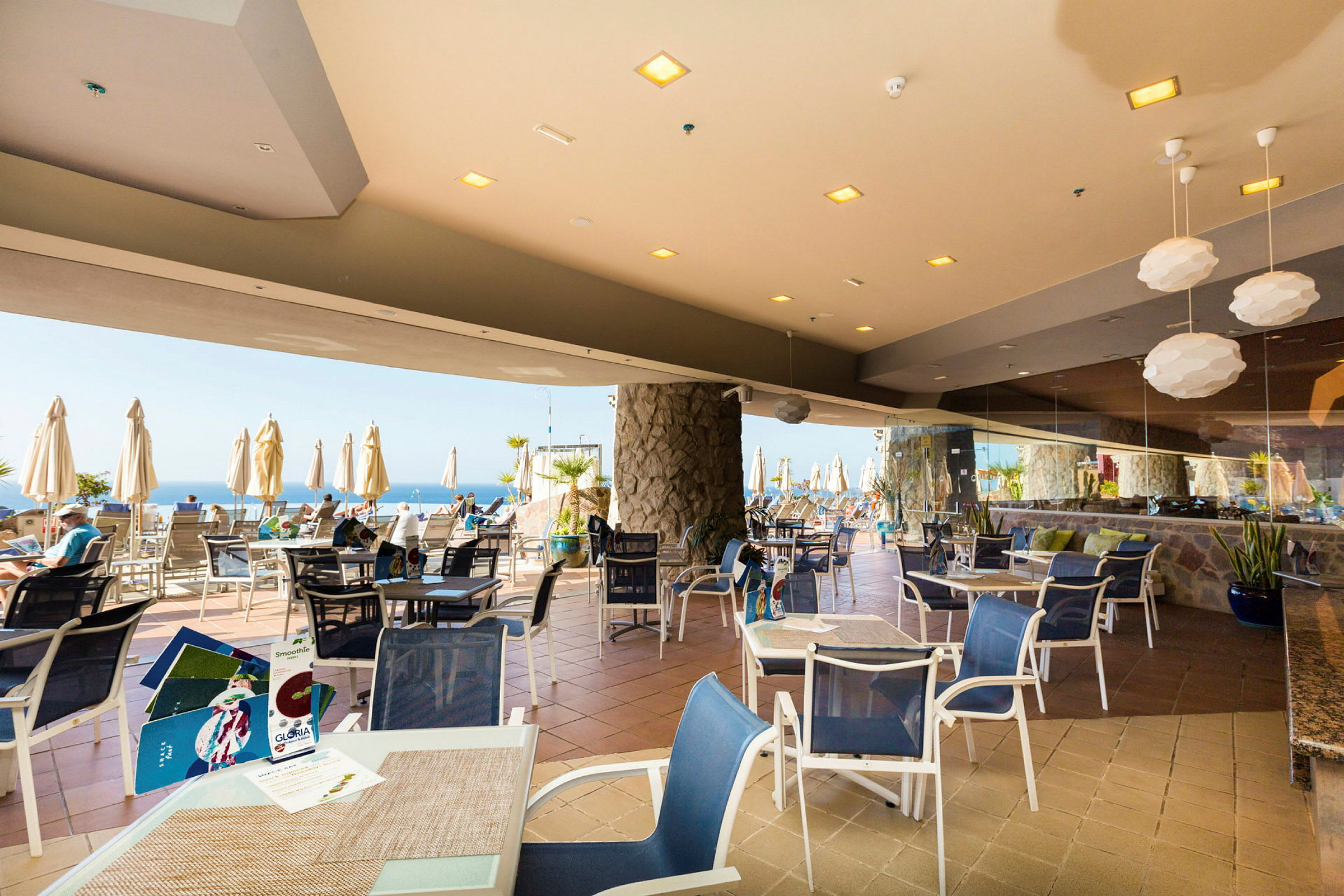 Restaurangtaverna med bord och stolar samt utsikt mot havet. (AI-genererad text)