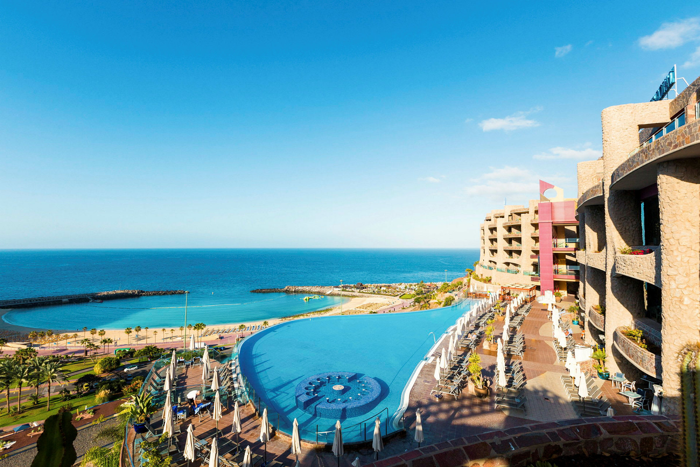 Bild av en stor infinitypool vid ett hotell med utsikt över havet och en sandstrand. (AI-genererad text)