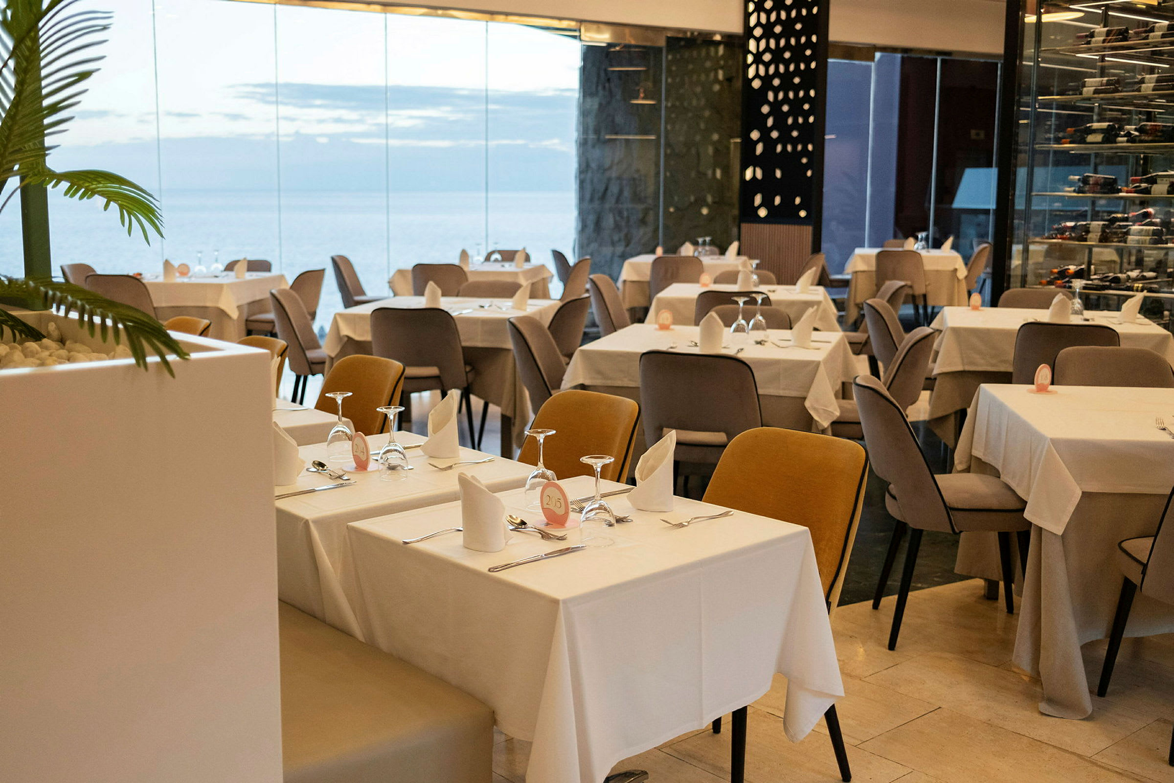 Restaurang med dukade bord och stolar i en modern miljö med glasväggar. (AI-genererad text)