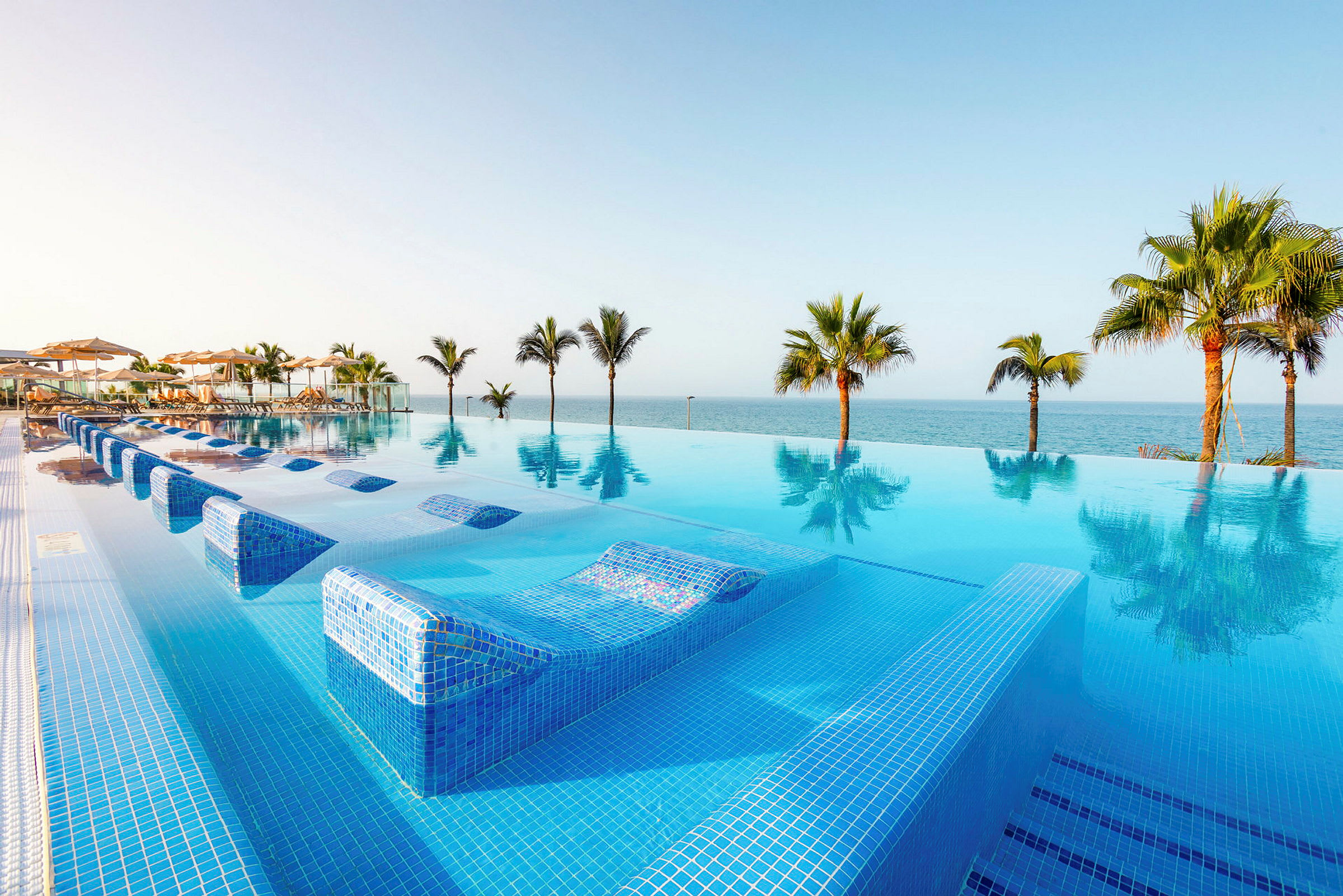 En infinitypool med utsikt över havet och omgivande palmer. (AI-genererad text)
