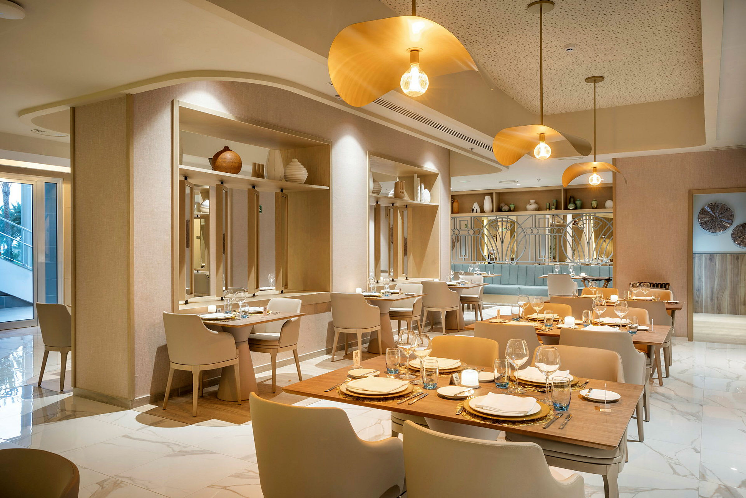 En elegant och modern restaurang med träbord, ljusa stolar och gyllene belysningsarmaturer. (AI-genererad text)