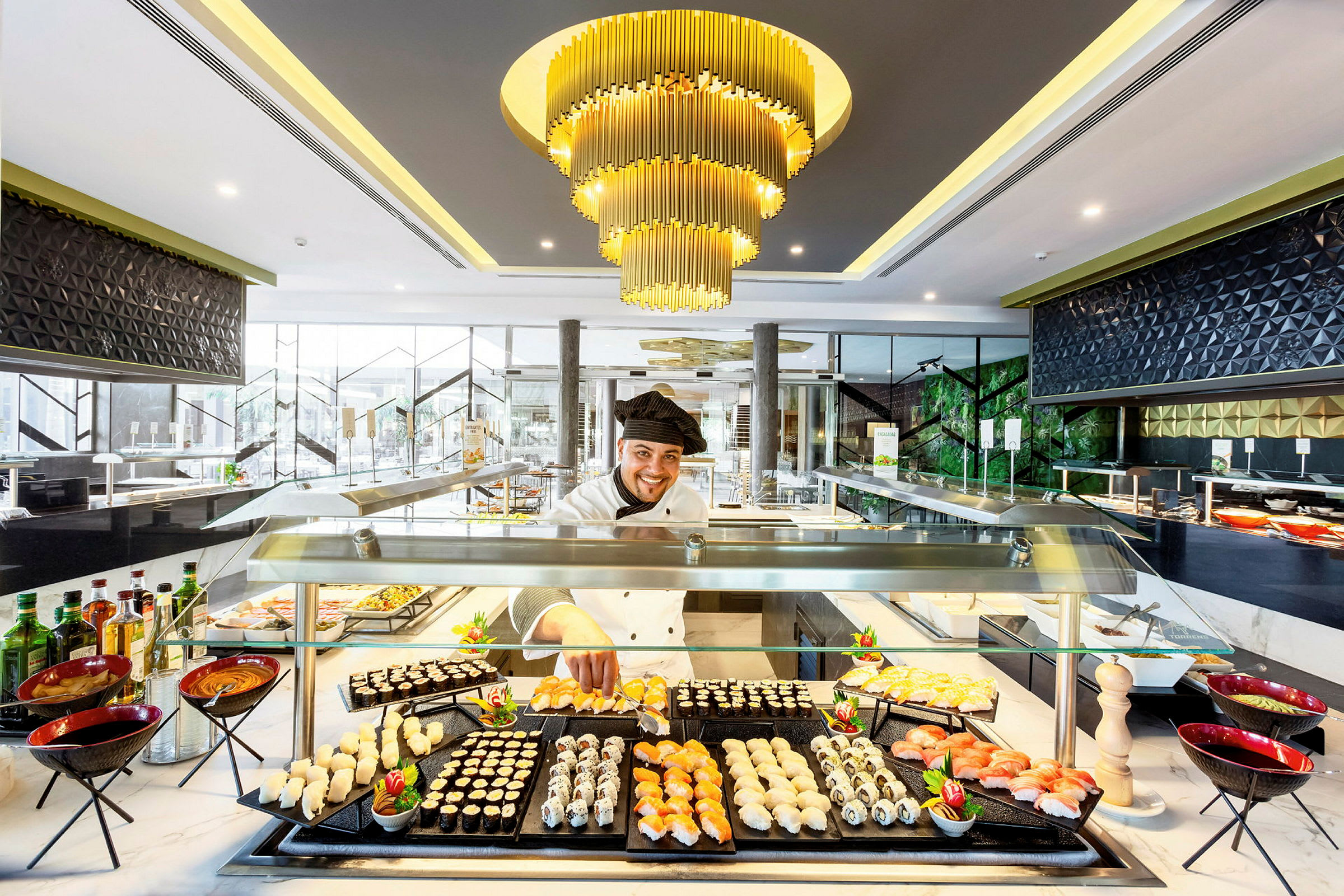 En elegant matservering med sushi och andra tilltugg på en buffé, belyst av en lyxig ljuskrona. (AI-genererad text)