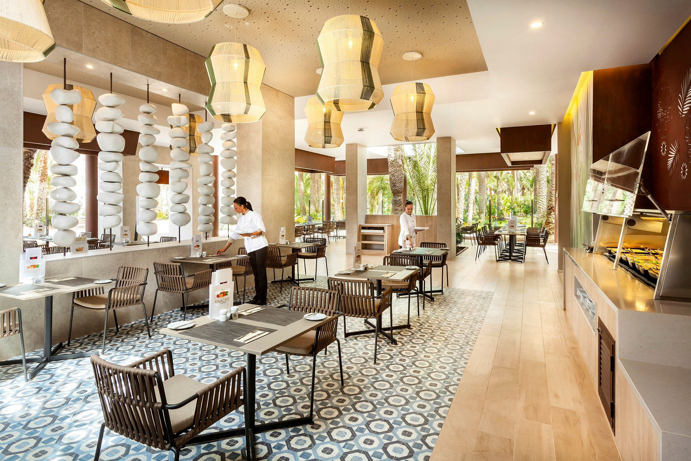 En modern restaurang med stora fönster, träbord och bekväma stolar, samt dekorativa taklampor och stenformationer. (AI-genererad text)