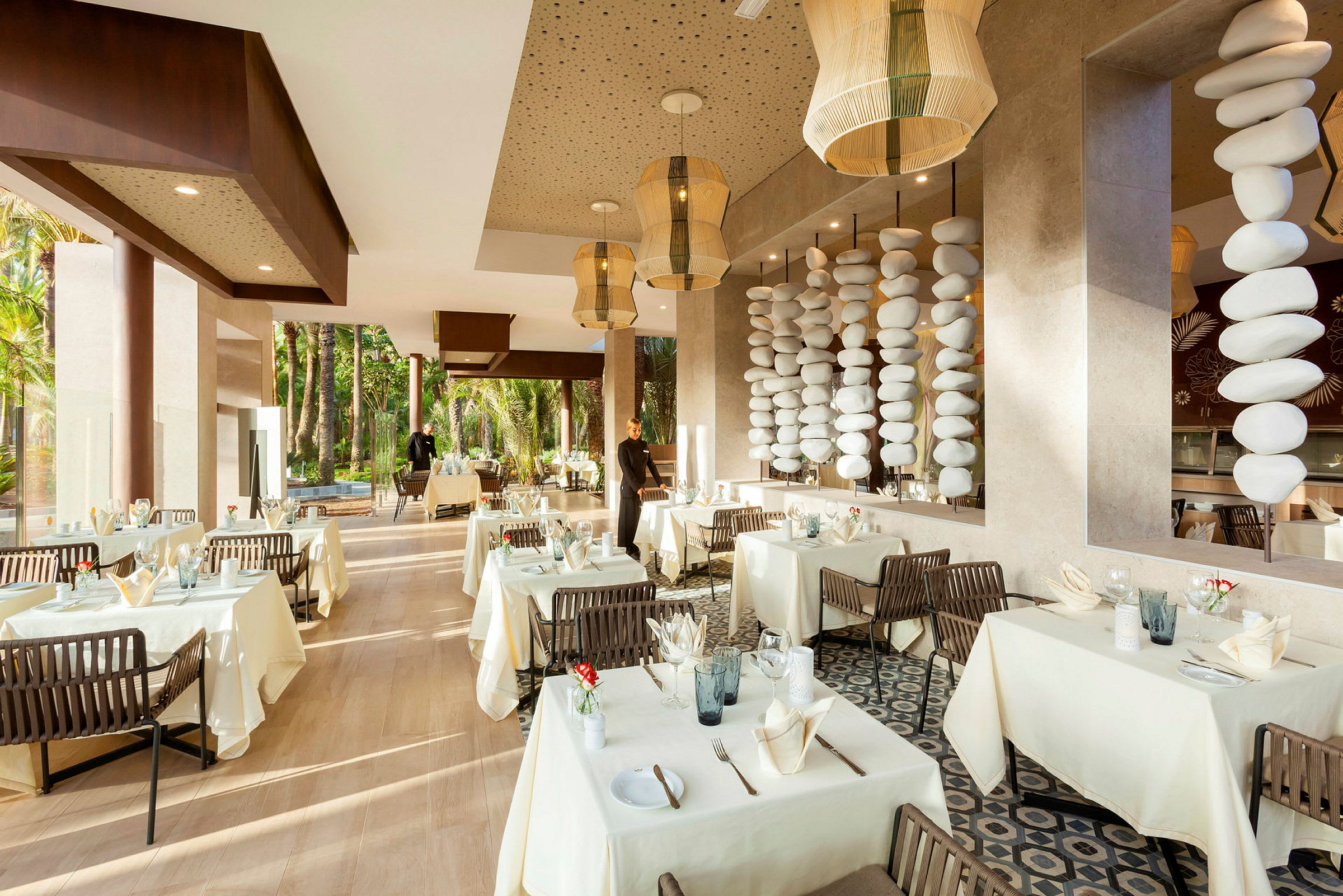 En elegant restaurang med vita dukar, dekorerade bord och stora fönster mot grönska. (AI-genererad text)