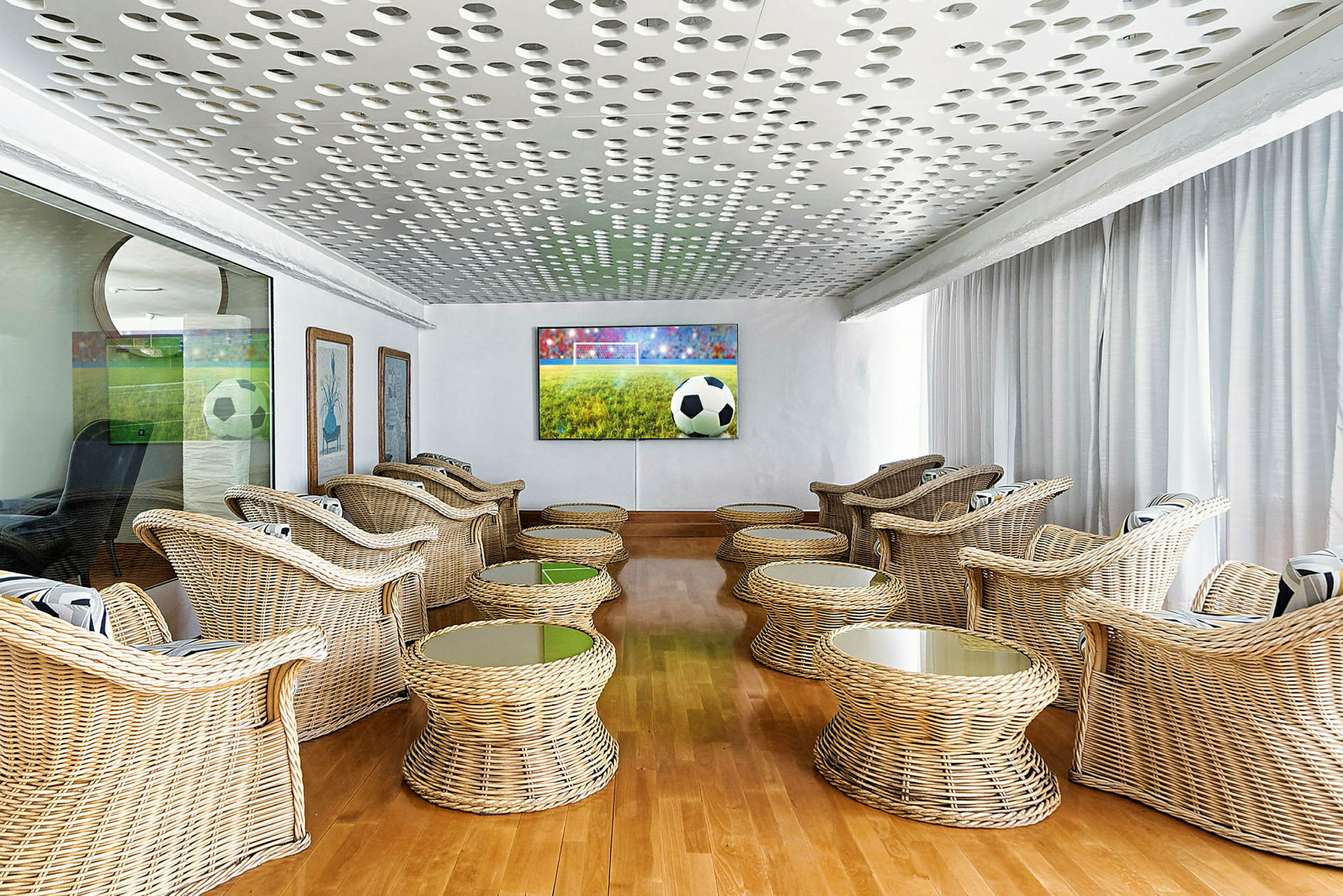 En lounge med rottingmöbler och en stor TV-skärm som visar en fotbollsmatch. (AI-genererad text)