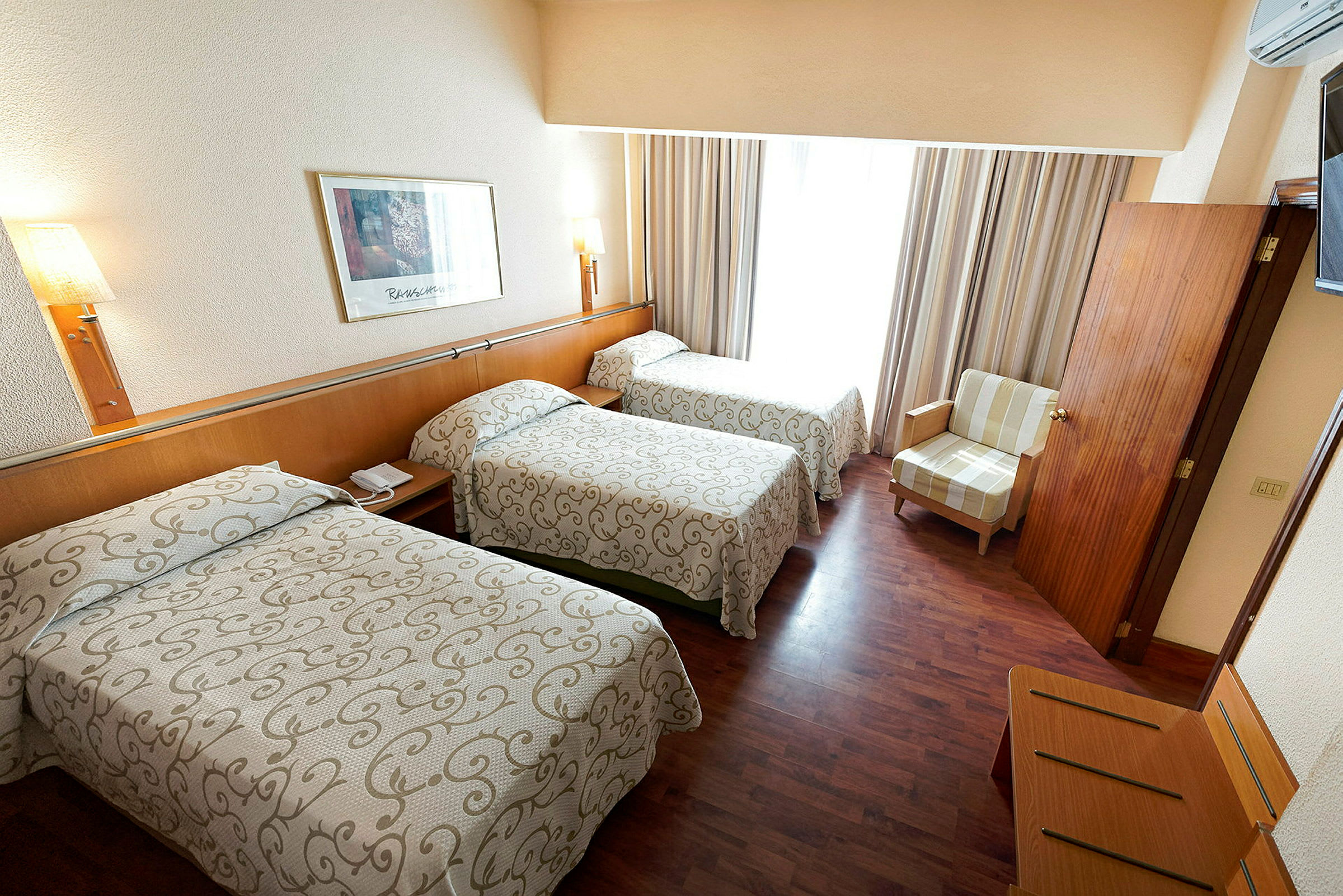 Hotellrum med tre enkelsängar, en fåtölj och trägolv. (AI-genererad text)