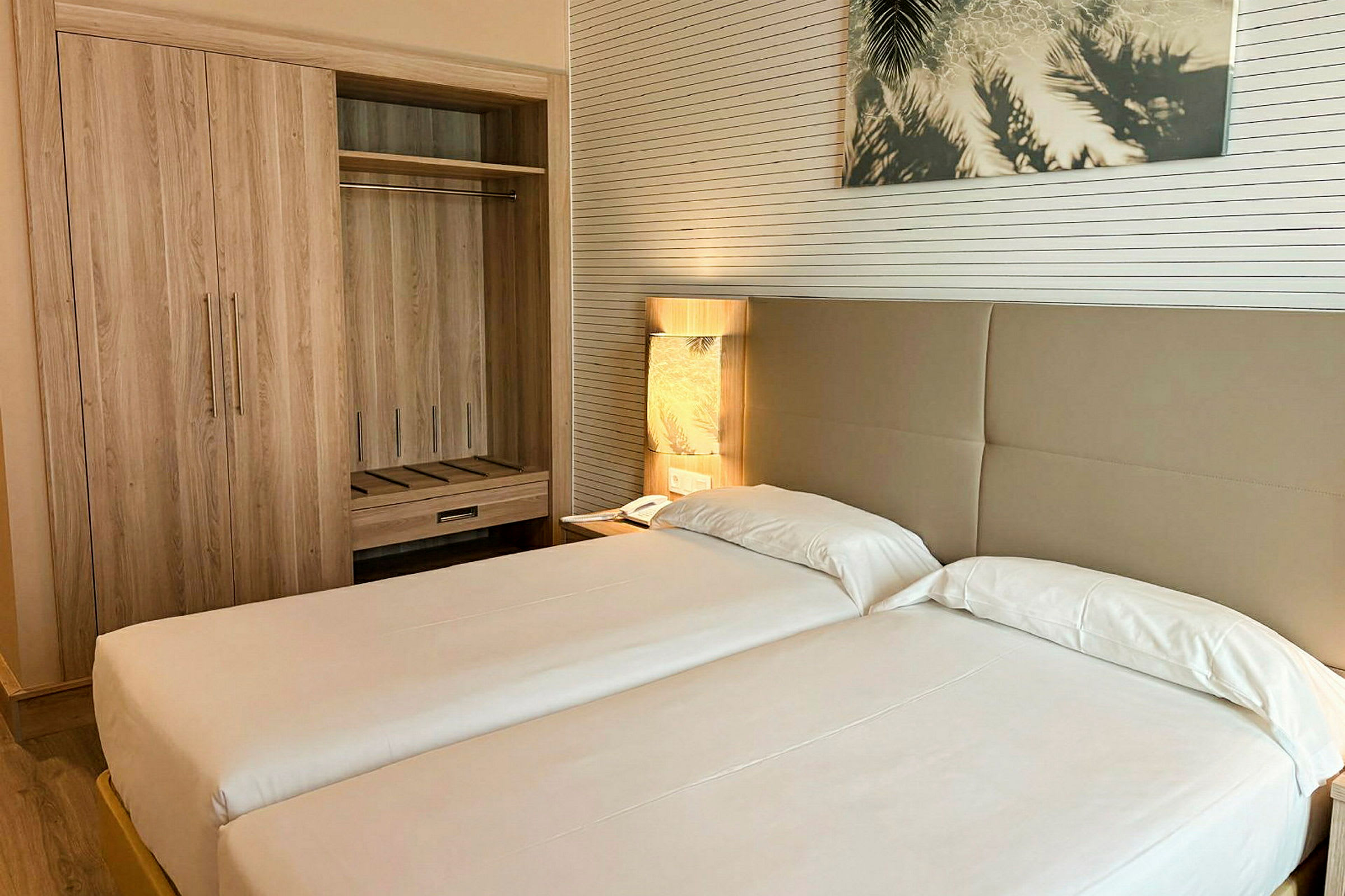 Hotellrum med två enkelsängar, ett garderobsskåp och en bordslampa intill sängen. (AI-genererad text)
