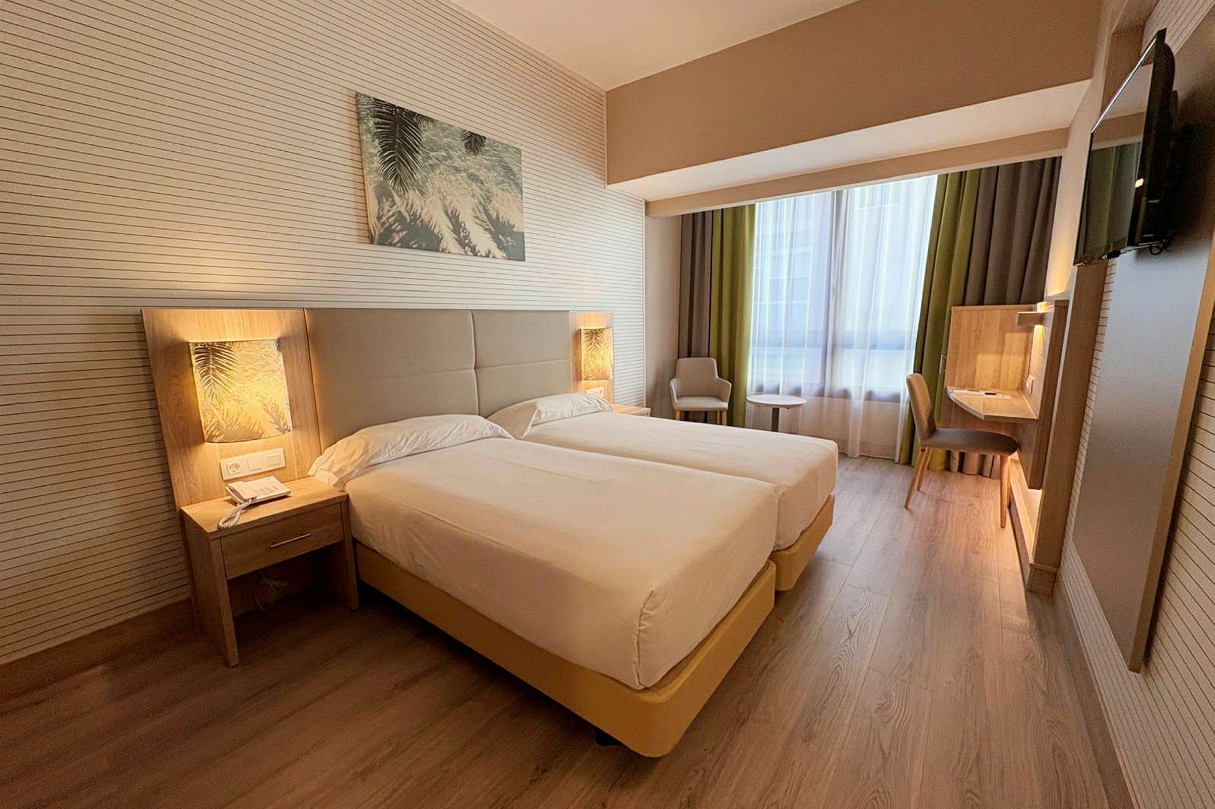 Ett hotellrum med två enkelsängar, nattduksbord, en arbetsyta och en fåtölj bredvid ett fönster. (AI-genererad text)