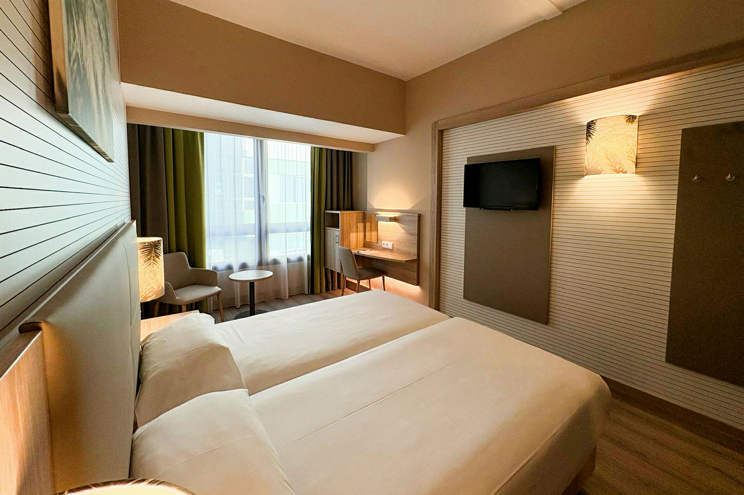 Ett hotellrum med två enkelsängar, en arbetsplats, en stol och ett bord nära ett stort fönster. (AI-genererad text)