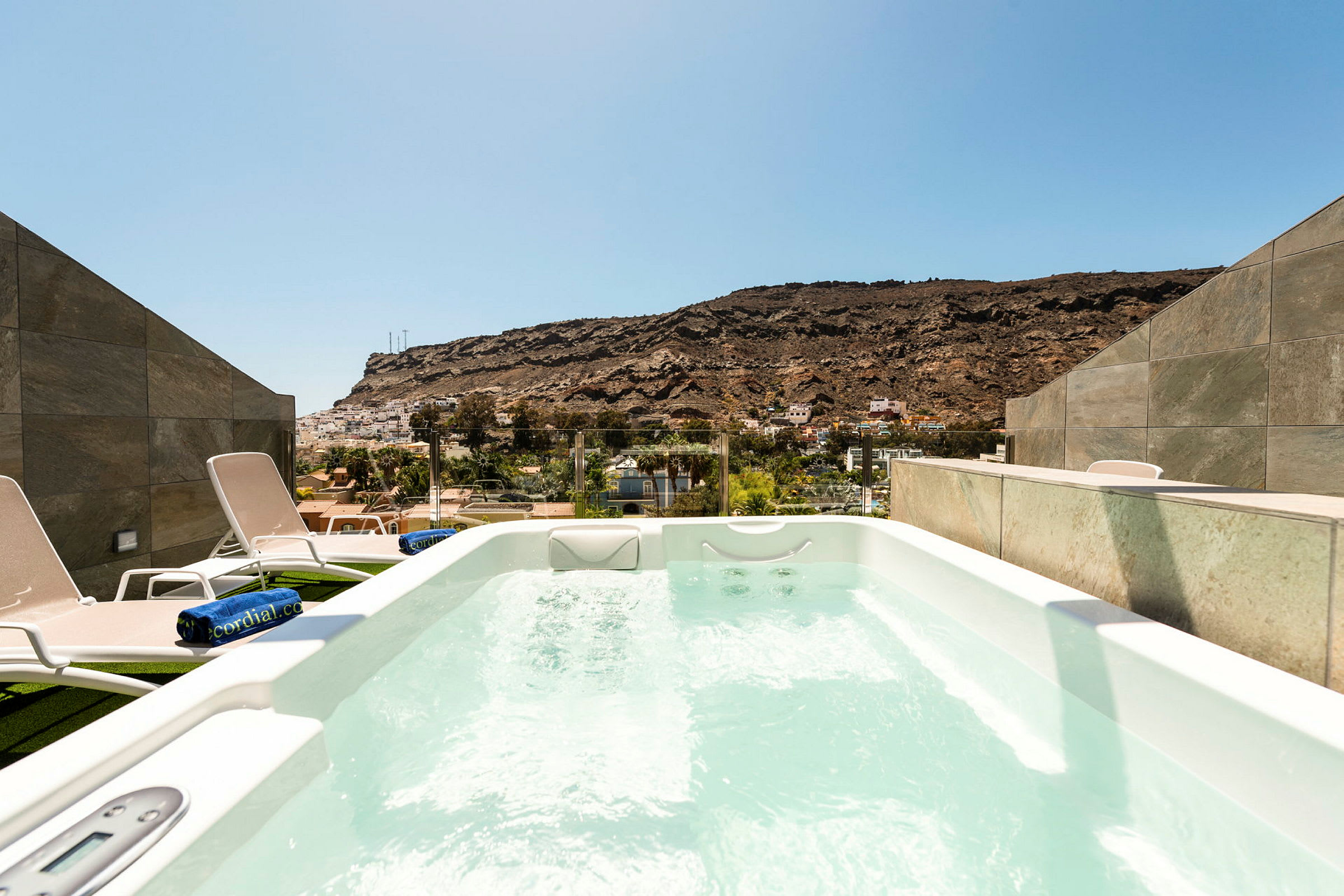 Utomhusjacuzzi med utsikt över landskap med berg och byggnader. (AI-genererad text)