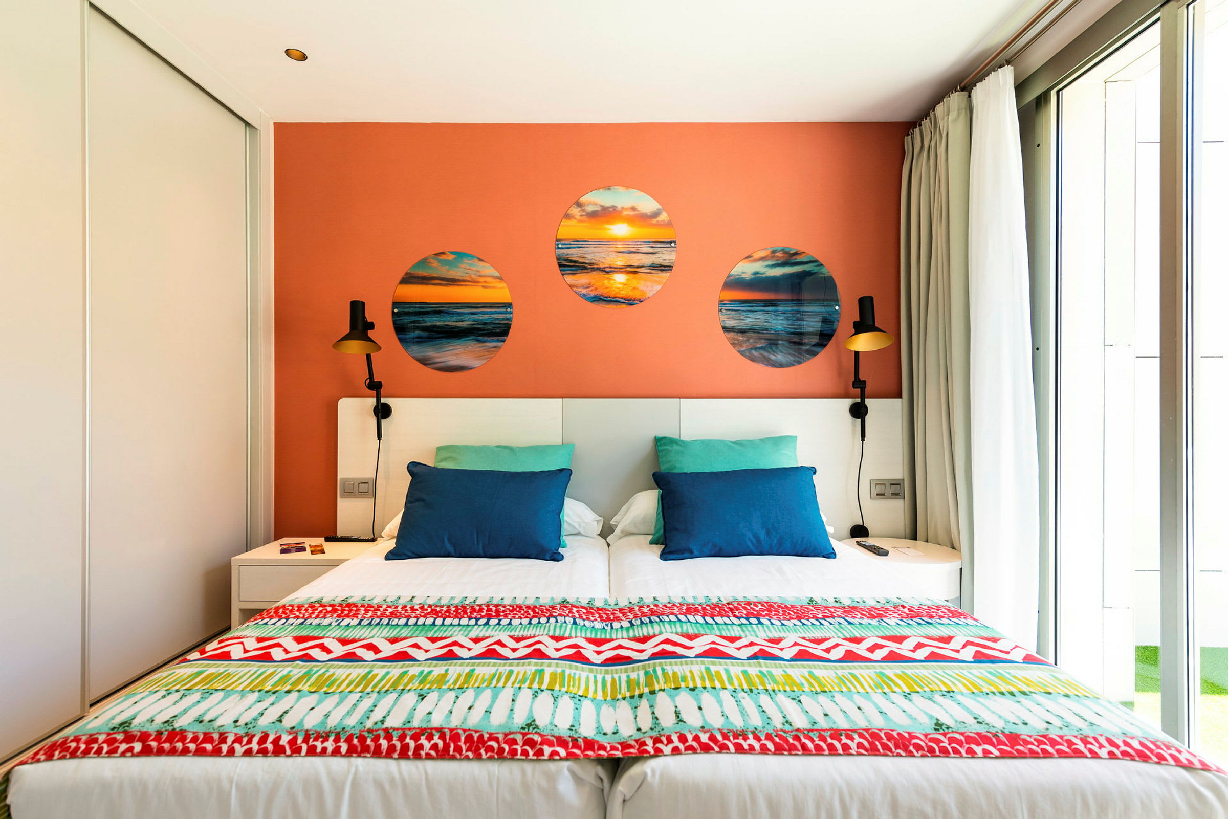 Ett hotellrum med en dubbelsäng, färgglada kuddar och en dekorativ orange vägg. (AI-genererad text)