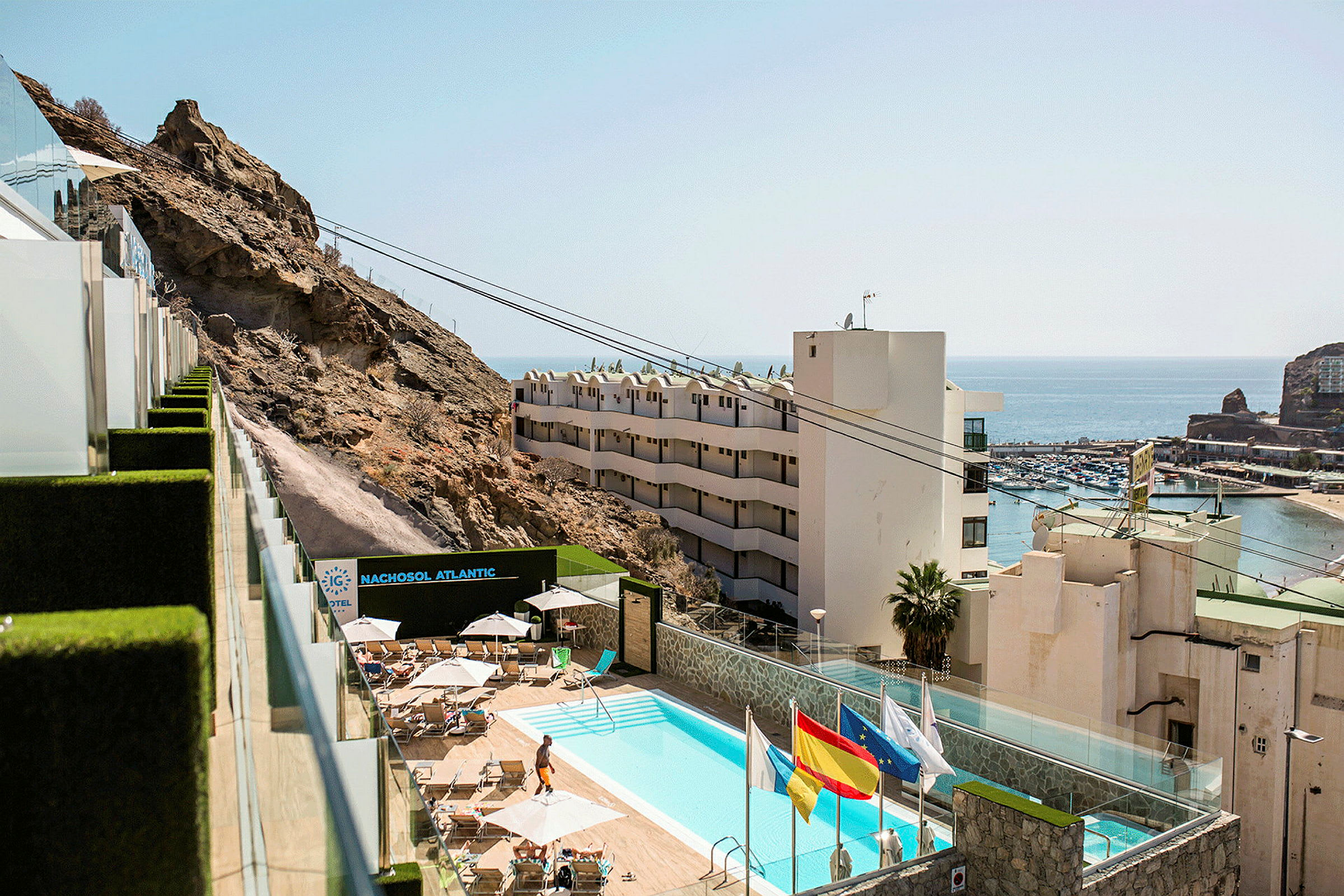 Utsikt över hotellområde med pool, berg och hamn. (AI-genererad text)